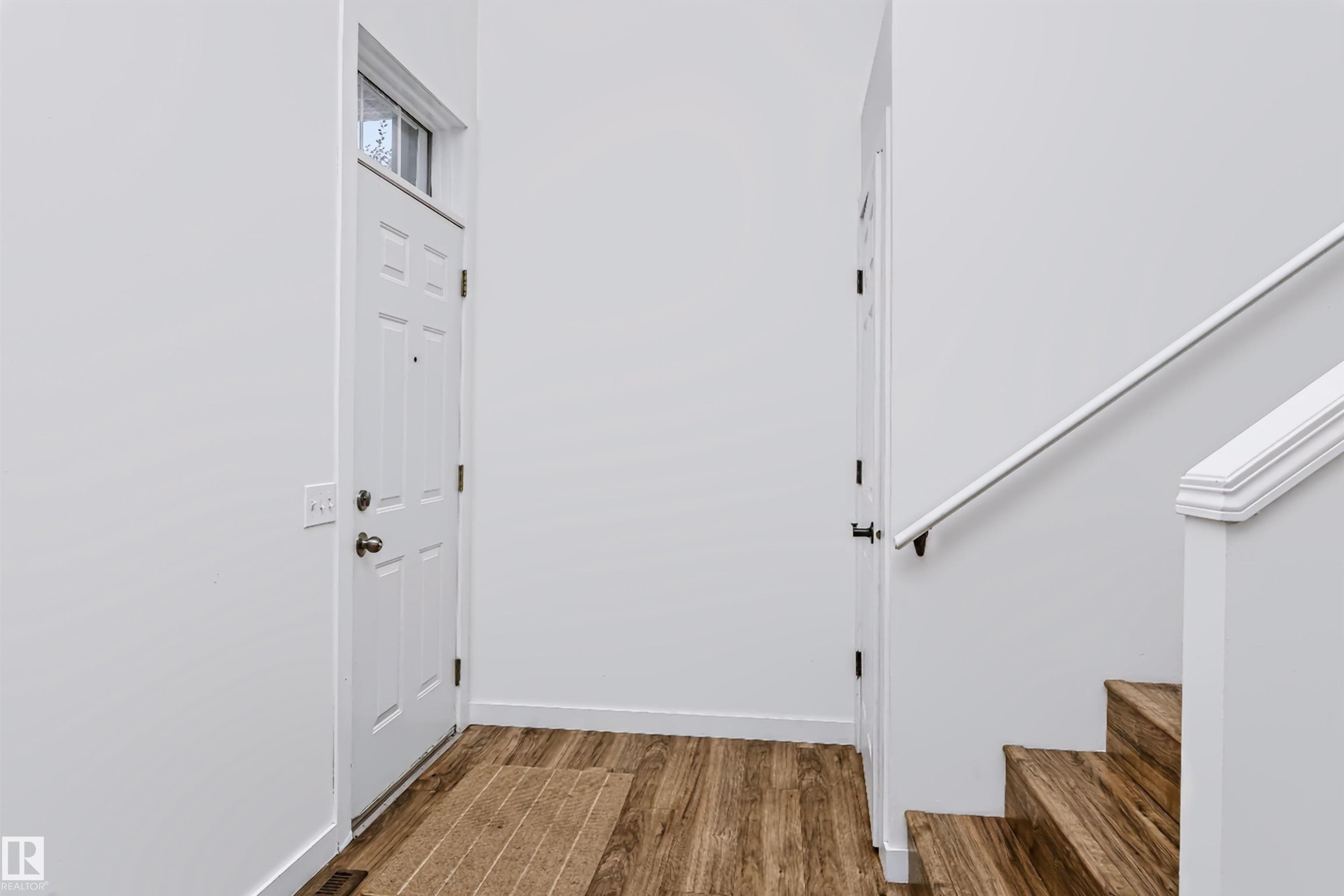 Entryway featuring wood-finish flooring, a white paneled door with transom window, and a staircase with wood-finish treads and white railing - #66 8304 11 Av Sw, Edmonton, AB - Indoor Photo Showing Other Room