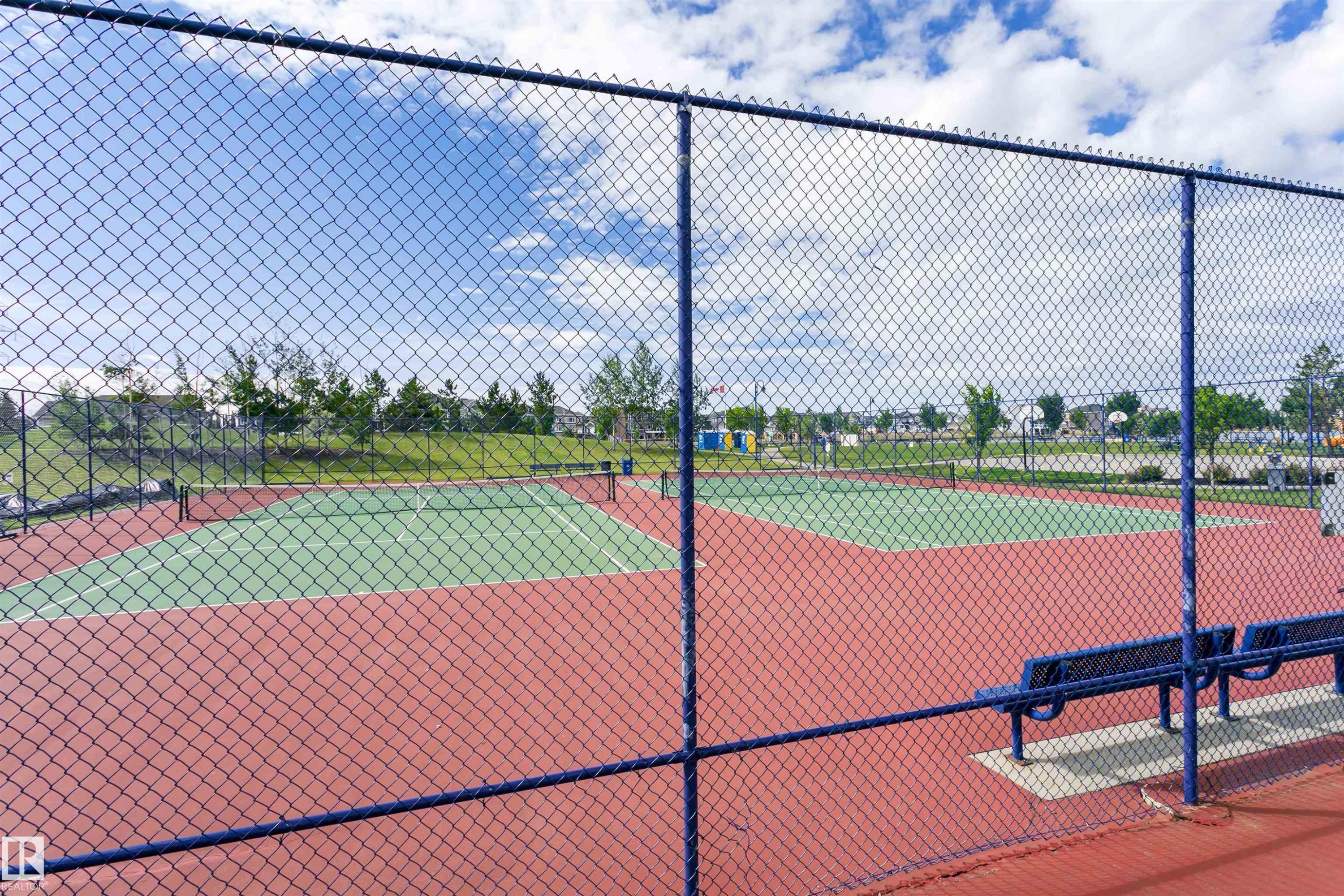Tennis court featuring a hard surface, red and green playing area, chain-link fencing, and integrated benches - #66 8304 11 Av Sw, Edmonton, AB - Outdoor With Deck Patio Veranda