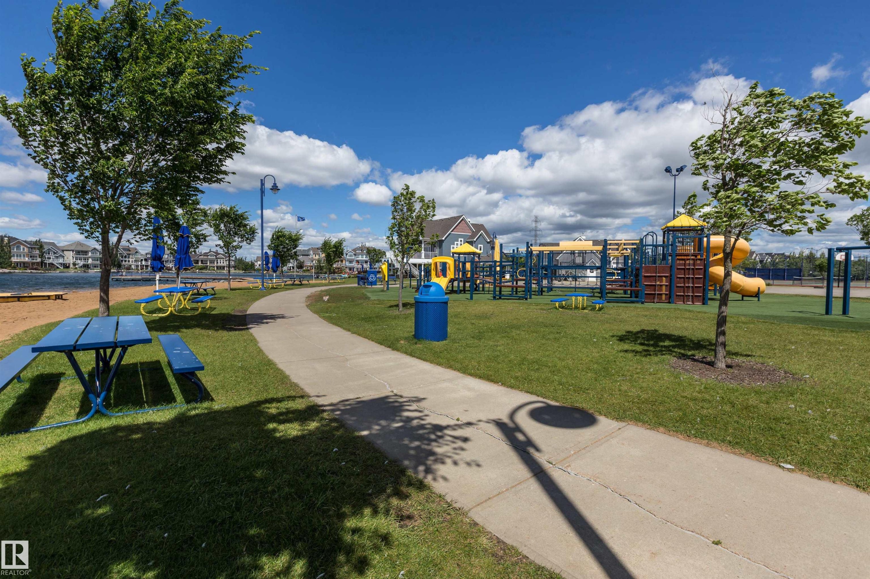 Recreational park area featuring a concrete pathway, mature trees, and a sand beach by the water - #66 8304 11 Av Sw, Edmonton, AB - Outdoor With View