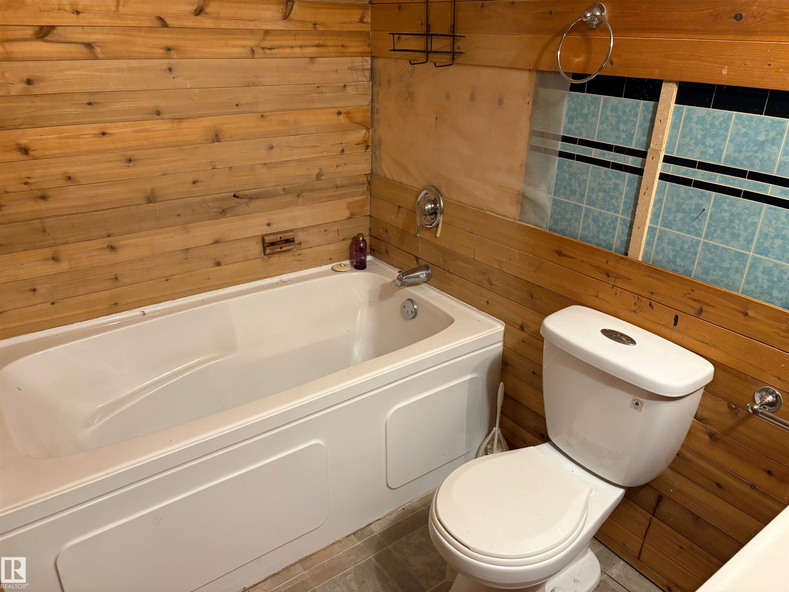 White bathtub with chrome fixtures, surrounded by horizontal wood paneling - 4620 Maria Drive, Smoky Lake Town, AB - Indoor Photo Showing Bathroom