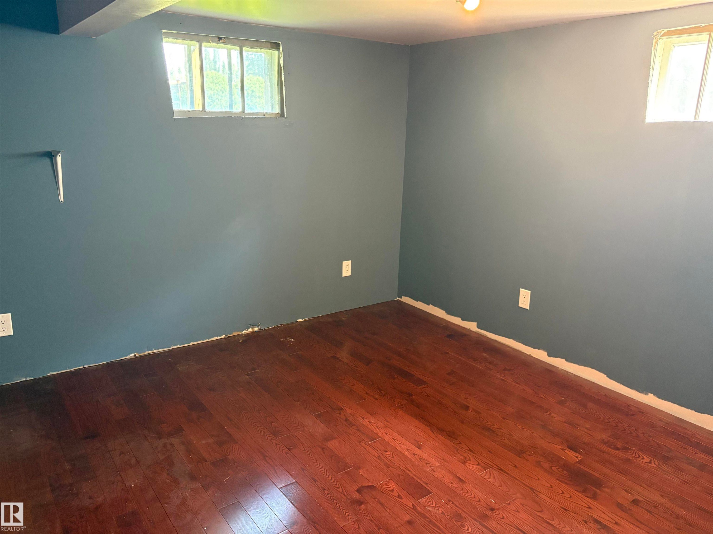 Spacious room featuring rich wood-finish flooring, contemporary blue-gray wall paint, and two distinct windows - 4620 Maria Drive, Smoky Lake Town, AB - Indoor Photo Showing Other Room