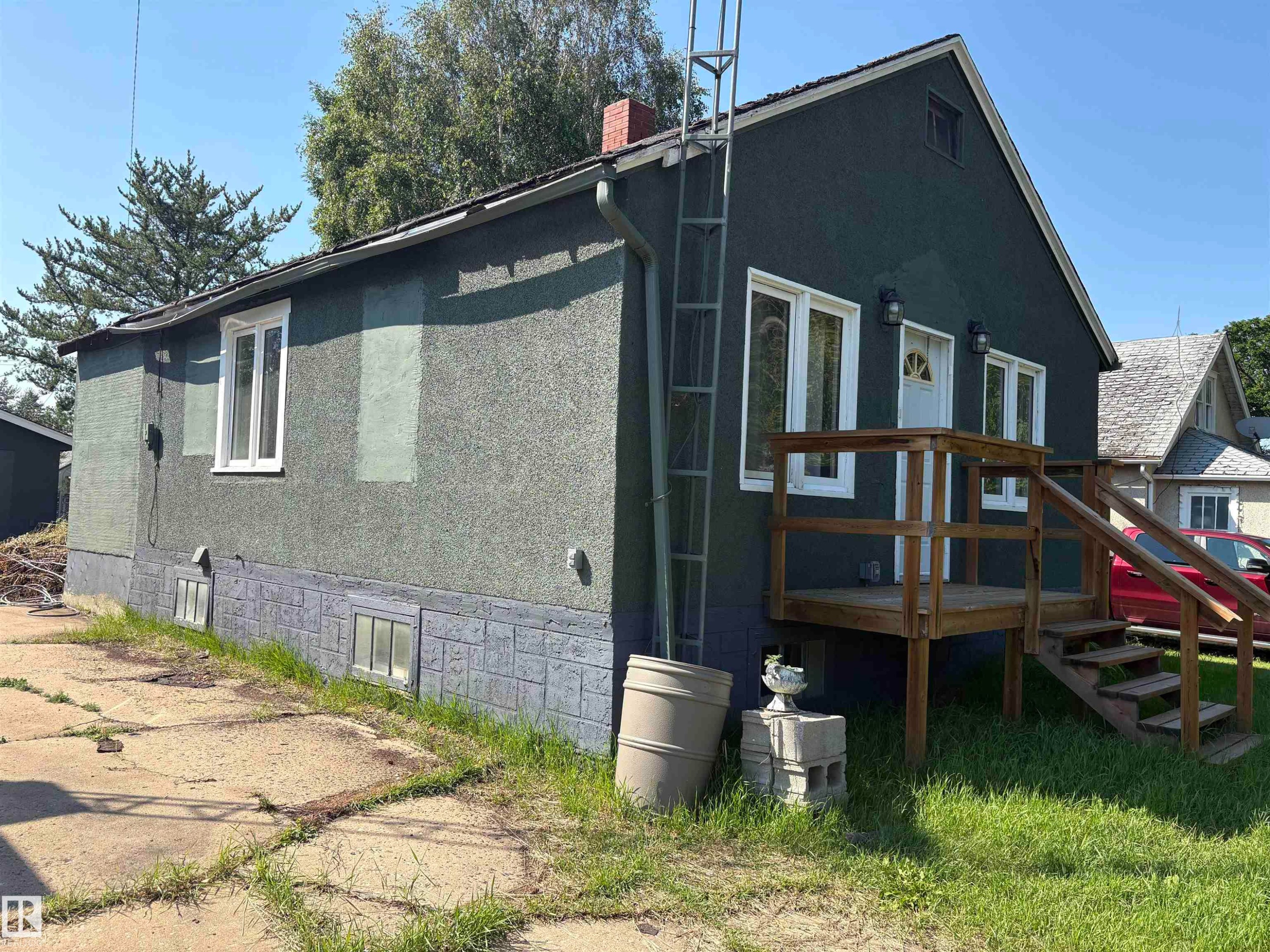 stucco exterior featuring white-framed windows, a wood deck with stairs, a white entry door, and two exterior wall-mounted light fixtures - 4620 Maria Drive, Smoky Lake Town, AB - Outdoor