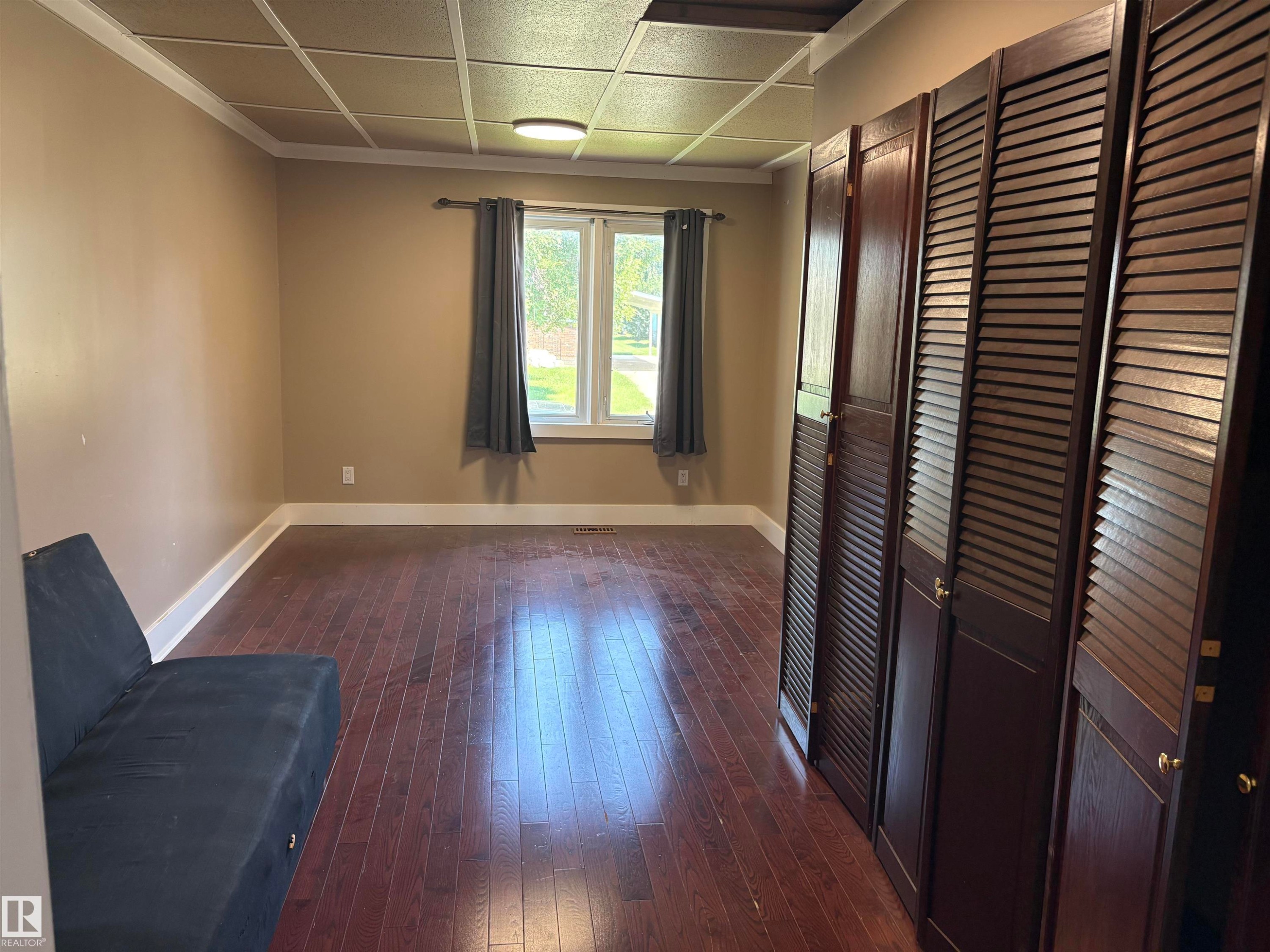 Spacious bedroom featuring hardwood flooring, a window with natural light, and a grid-patterned ceiling - 4620 Maria Drive, Smoky Lake Town, AB - Indoor Photo Showing Other Room