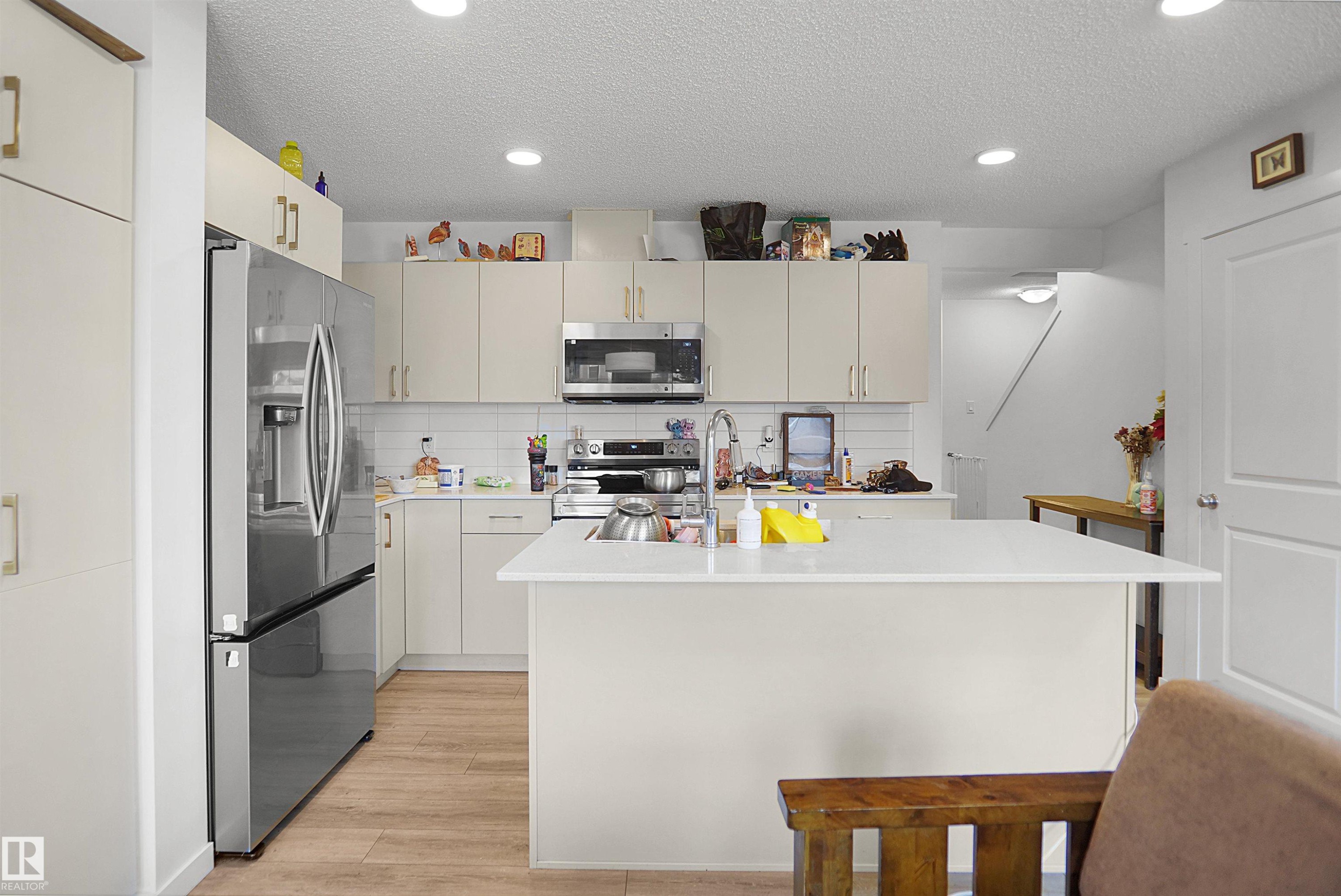 Modern kitchen featuring a central island, recessed lighting, wood-finish flooring, white subway tile backsplash, and stainless steel appliances - #42 19904 31 Av Nw, Edmonton, AB - Indoor Photo Showing Kitchen