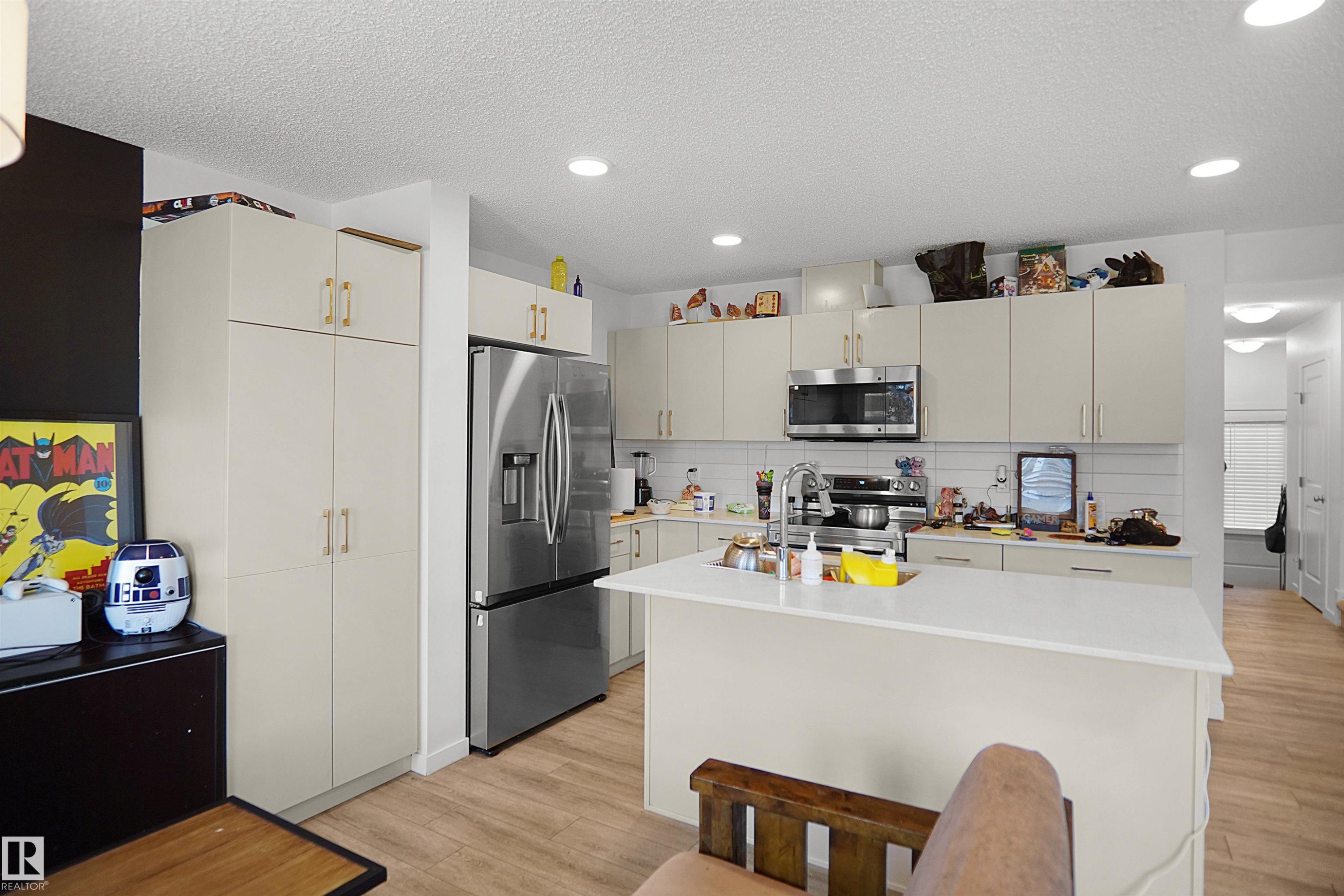 Kitchen featuring light-toned cabinetry, stainless steel appliances, a center island with a sink, recessed lighting, and wood-finish flooring - #42 19904 31 Av Nw, Edmonton, AB - Indoor Photo Showing Kitchen