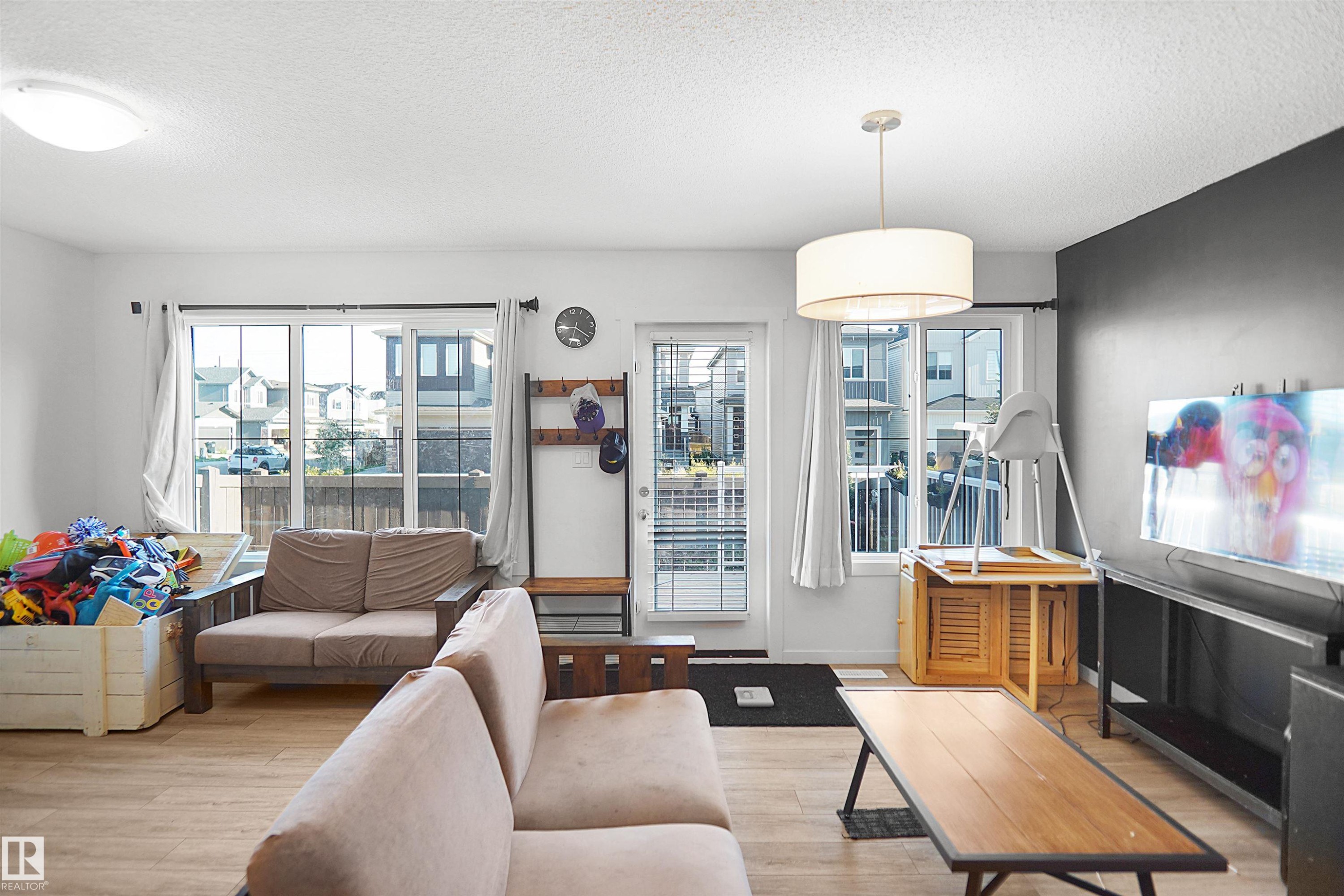 Living area featuring light wood-finish flooring, white walls, and a partial accent wall with a dark finish - #42 19904 31 Av Nw, Edmonton, AB - Indoor Photo Showing Living Room