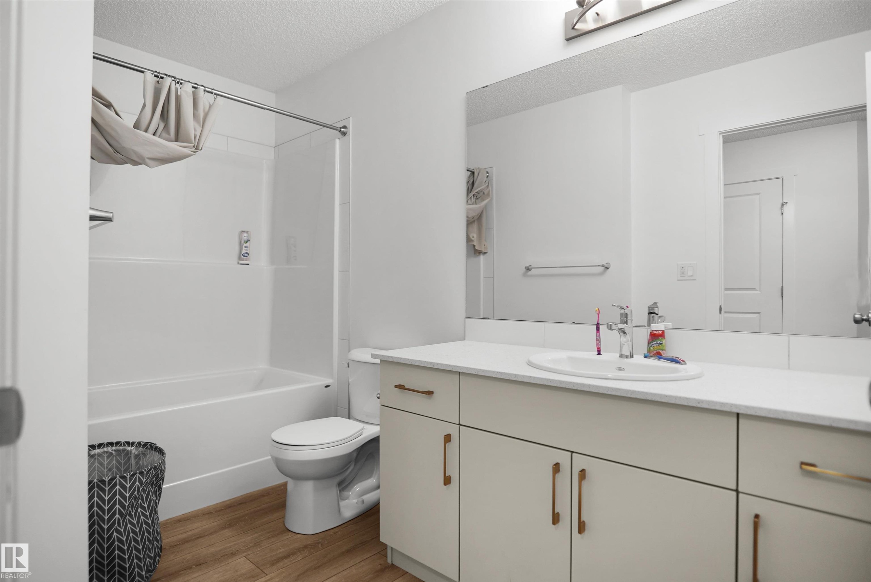 Bathroom featuring a tub/shower combination, light wood-finish flooring, a toilet, a vanity with an integrated sink, and a large wall-mounted mirror - #42 19904 31 Av Nw, Edmonton, AB - Indoor Photo Showing Bathroom
