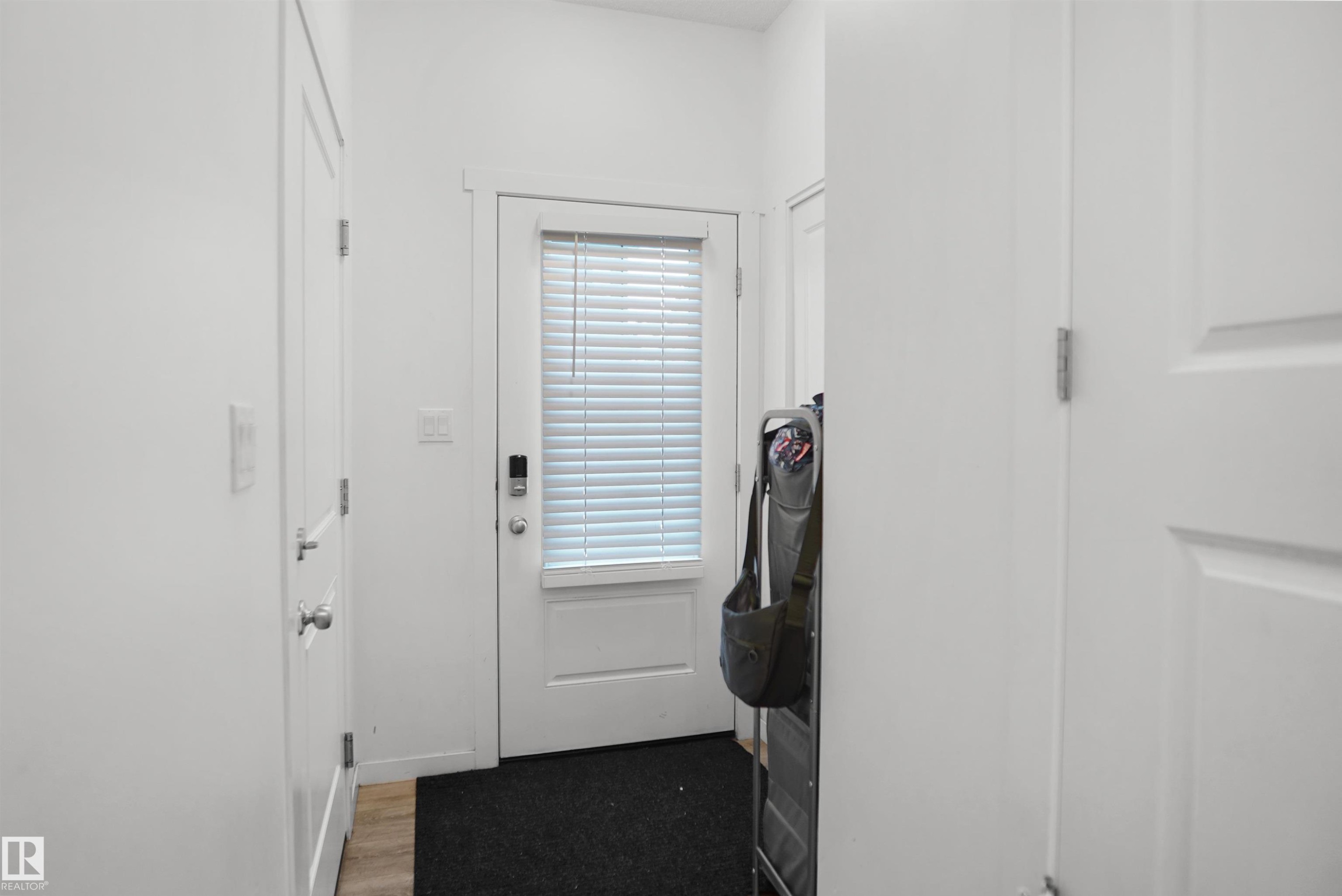 Entryway featuring a white paneled door with integrated window blinds, a smart lock, and wood-finish flooring - #42 19904 31 Av Nw, Edmonton, AB - Indoor Photo Showing Other Room