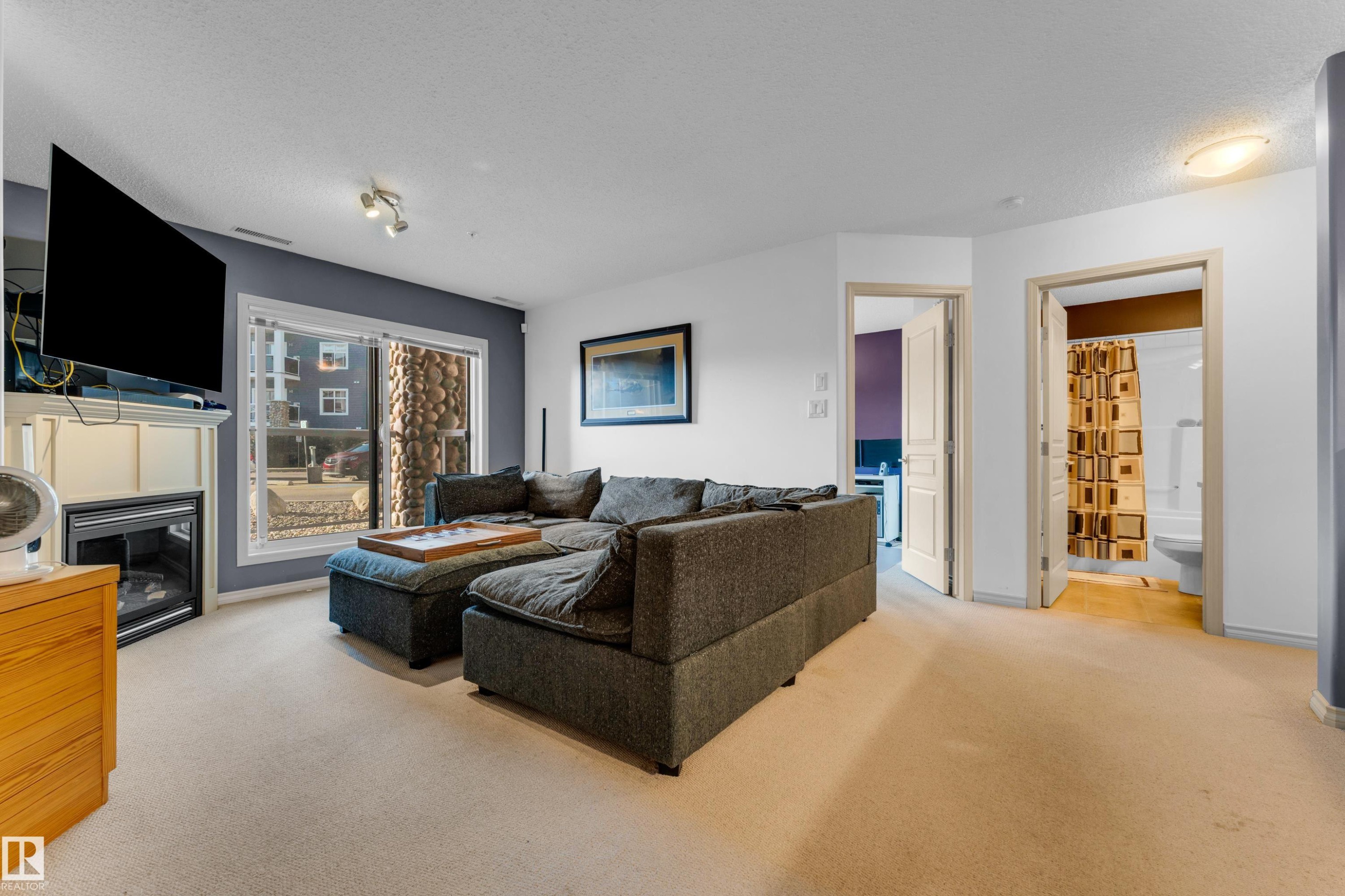 Living area featuring a fireplace with a white mantel, beige carpeting, and a sliding glass door - #136 16035 132 St Nw, Edmonton, AB - Indoor Photo Showing Living Room With Fireplace