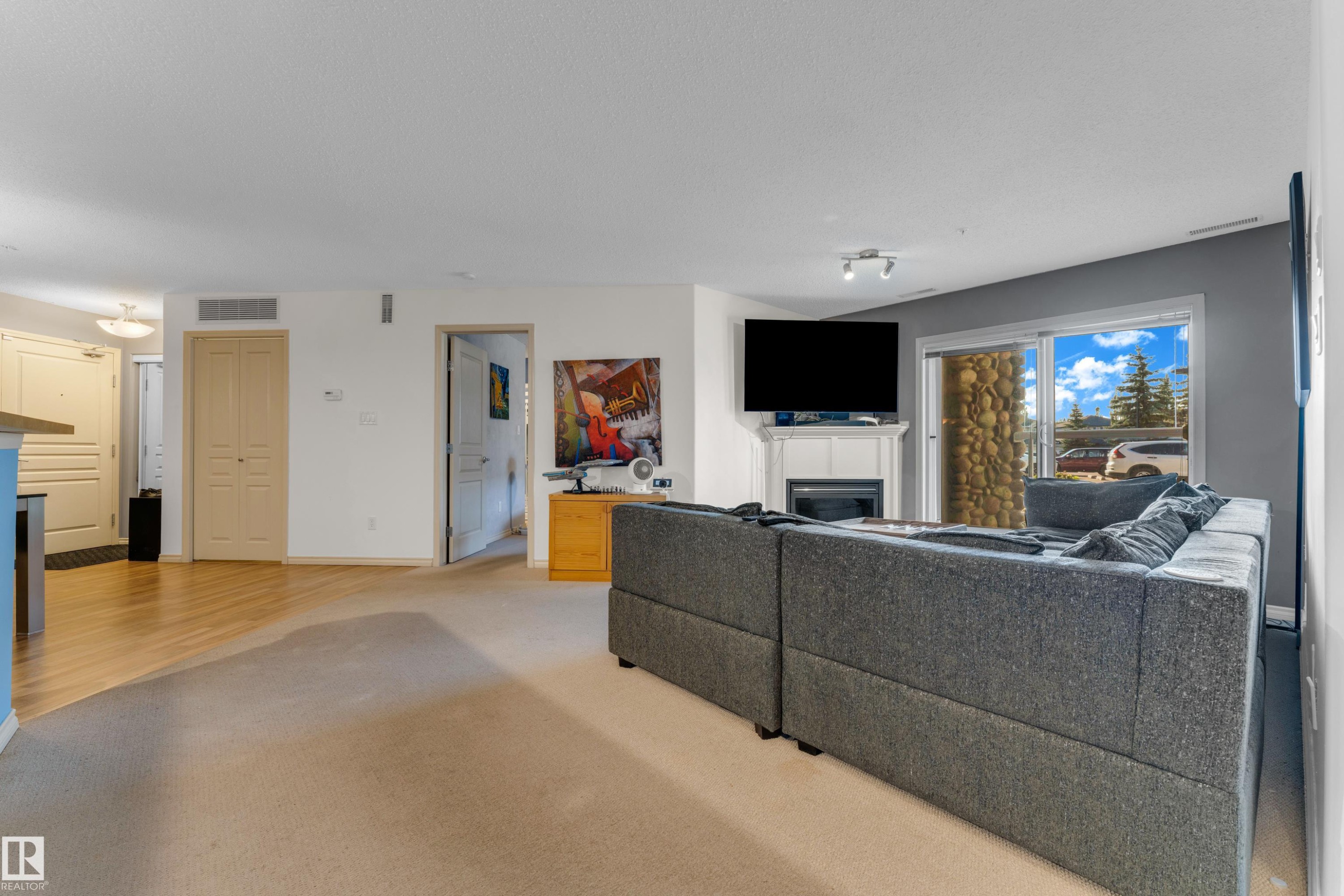 Living area featuring a white fireplace with mantle, sliding glass patio doors, and light wood-finish flooring transitioning to carpet - #136 16035 132 St Nw, Edmonton, AB - Indoor Photo Showing Living Room With Fireplace