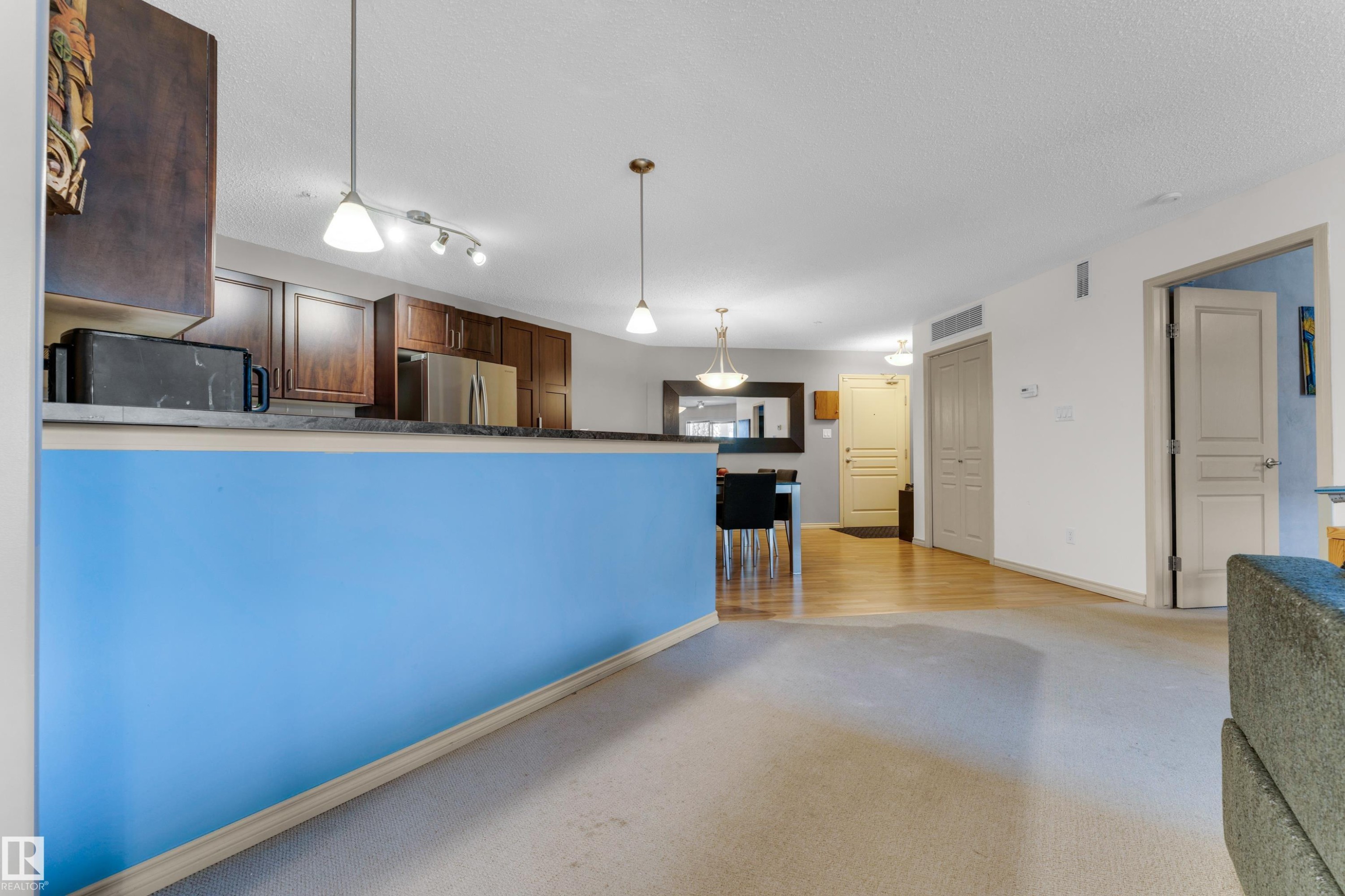 Open-concept living space featuring a carpeted area, hard surface flooring, and a kitchen with stainless steel appliances and wood cabinetry - #136 16035 132 St Nw, Edmonton, AB - Indoor
