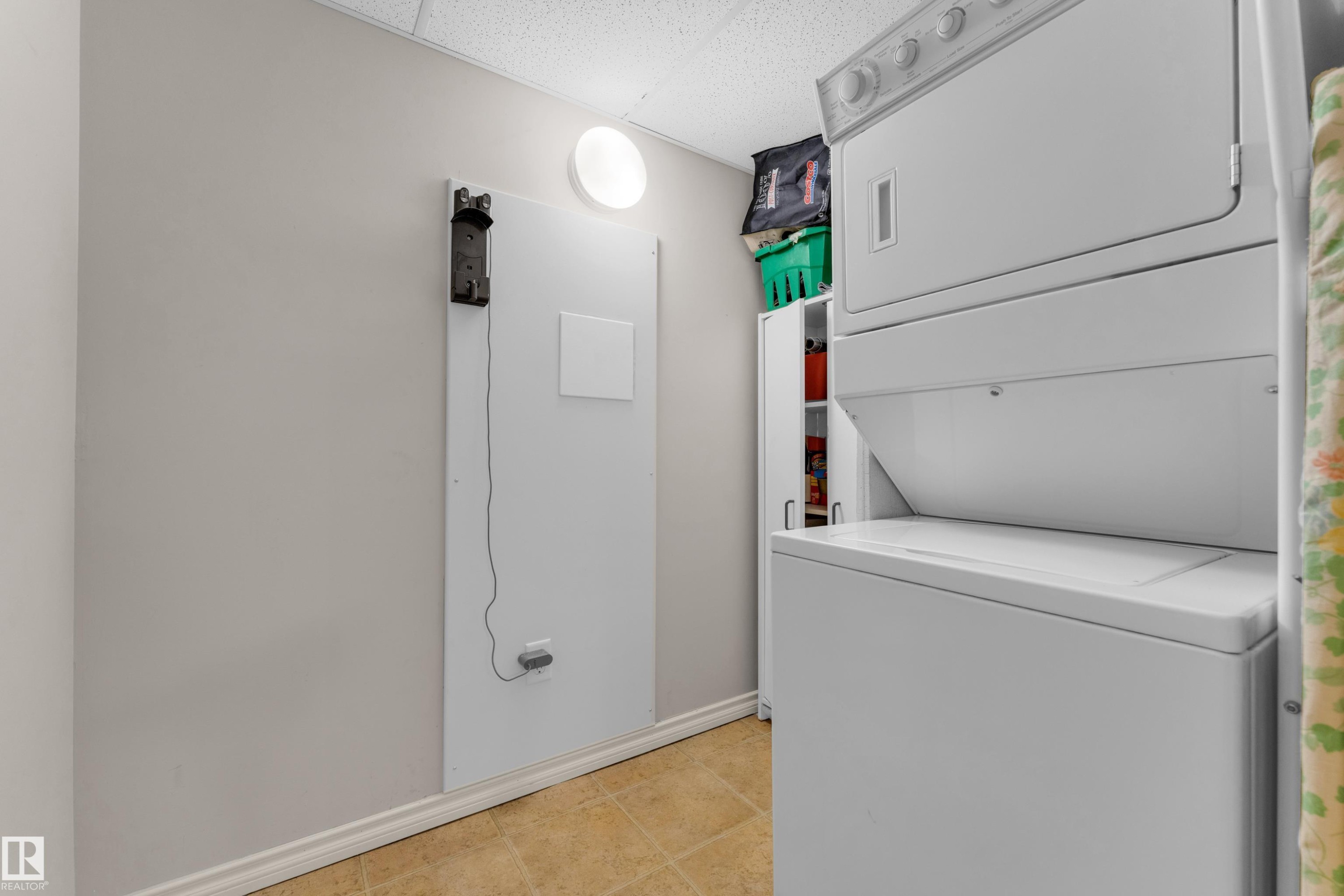 Dedicated utility area featuring a stacked washer and dryer, neutral wall paint, and tiled flooring - #136 16035 132 St Nw, Edmonton, AB - Indoor Photo Showing Laundry Room