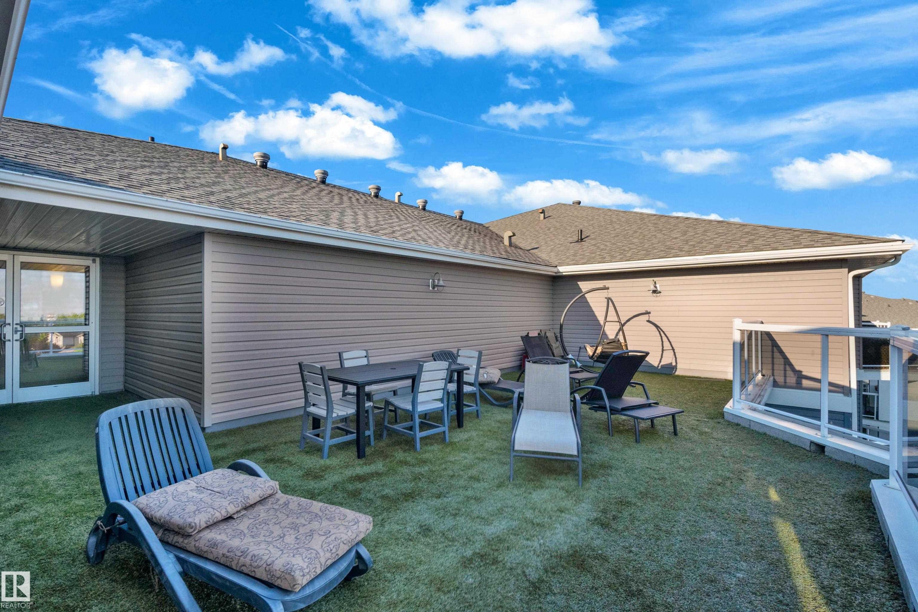 Rooftop deck featuring artificial turf, a glass safety barrier, and exterior wall sconces - #136 16035 132 St Nw, Edmonton, AB - Outdoor With Deck Patio Veranda With Exterior