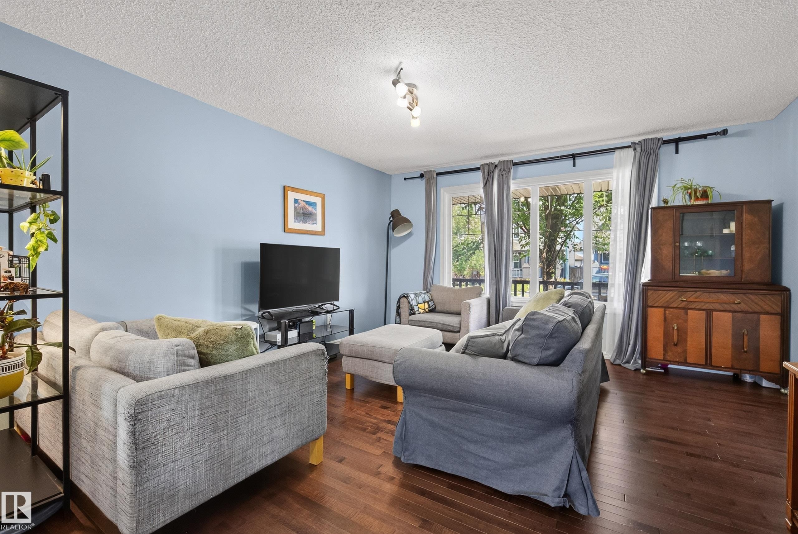 Spacious living area featuring rich wood-finish flooring, light blue wall paint, and substantial windows with natural light - 3003 20 Avenue Nw, Edmonton, AB - Indoor Photo Showing Living Room