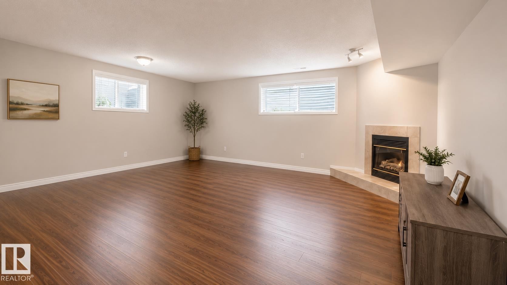 Spacious room featuring wood-finish flooring, light neutral wall paint, and a corner fireplace with a tile surround and hearth - 29 Campbell Road, Leduc, AB - Indoor With Fireplace