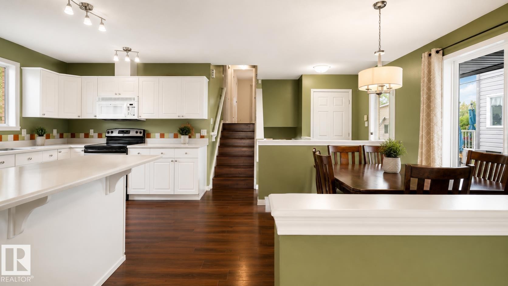 Kitchen and dining area featuring rich wood-finish flooring, white cabinetry, light countertops, and a full suite of black kitchen appliances - 29 Campbell Road, Leduc, AB - Indoor