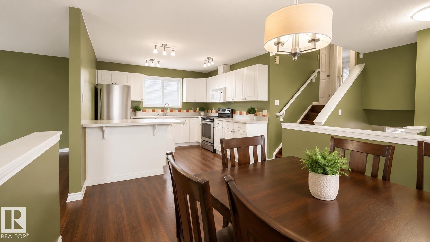 Open-concept kitchen and dining area featuring wood-finish flooring, white cabinetry, stainless steel appliances, a breakfast bar, and a drum-style ceiling light fixture - 29 Campbell Road, Leduc, AB - Indoor Photo Showing Other Room