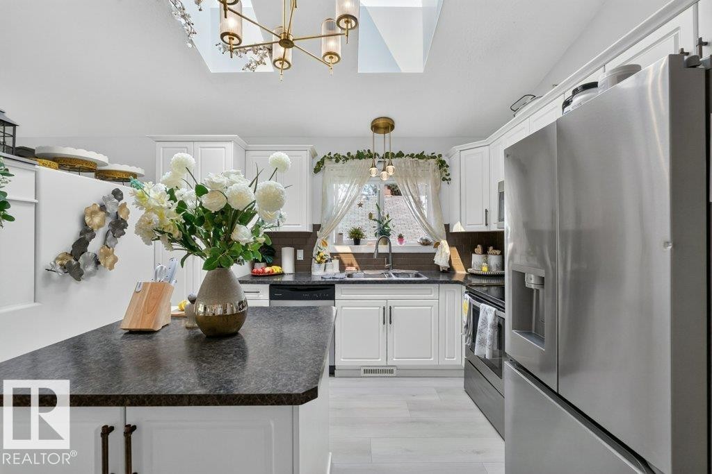 Kitchen featuring white cabinetry, dark countertops, skylights, and stainless steel appliances - 12219 89 Street Nw, Edmonton, AB - Indoor Photo Showing Kitchen With Double Sink
