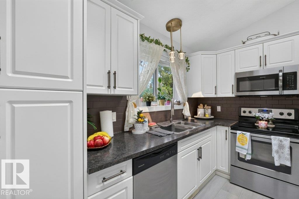 White shaker-style cabinetry with dark hardware, dark countertops, brown subway tile backsplash, and stainless steel appliances - 12219 89 Street Nw, Edmonton, AB - Indoor Photo Showing Kitchen With Double Sink