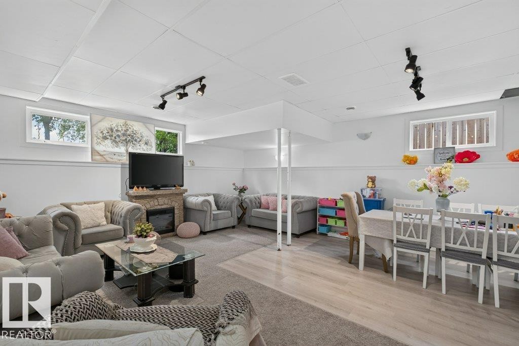 Spacious lower level featuring a stone-clad fireplace, track lighting, wood-finish flooring, and multiple windows - 12219 89 Street Nw, Edmonton, AB - Indoor