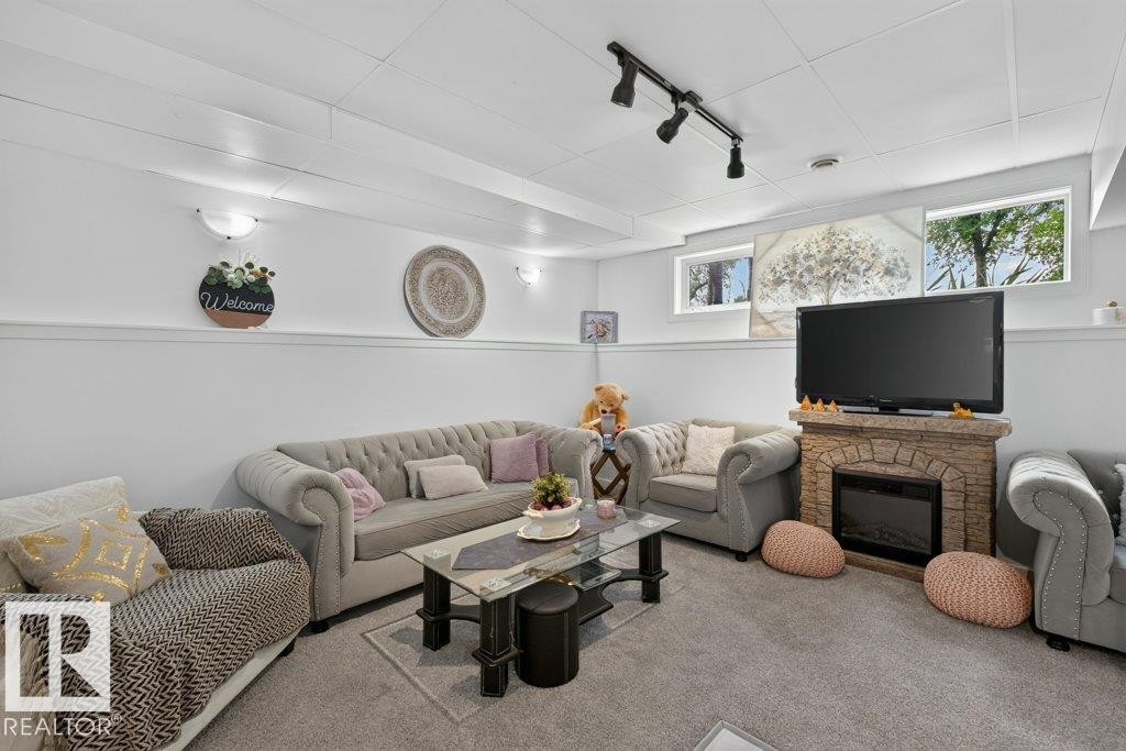 Carpeted living area featuring a stone-look fireplace with an electric insert, recessed lighting, and wall-mounted sconces - 12219 89 Street Nw, Edmonton, AB - Indoor Photo Showing Living Room