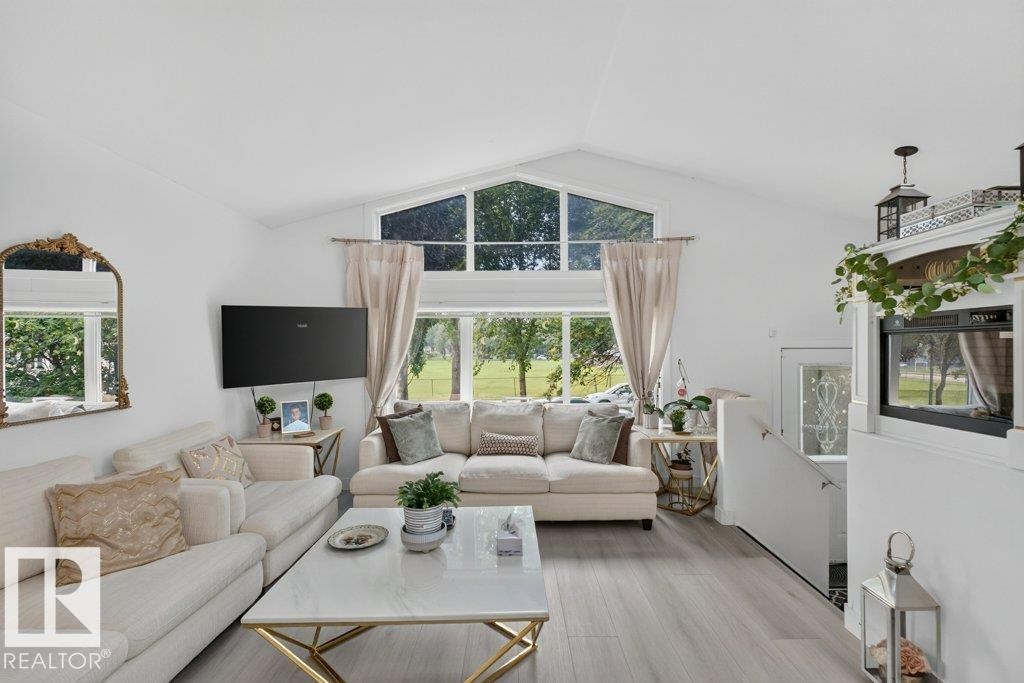 Vaulted ceiling living area featuring large windows, light wood-finish flooring, a contemporary white and gold coffee table, and a built-in electric fireplace - 12219 89 Street Nw, Edmonton, AB - Indoor Photo Showing Living Room
