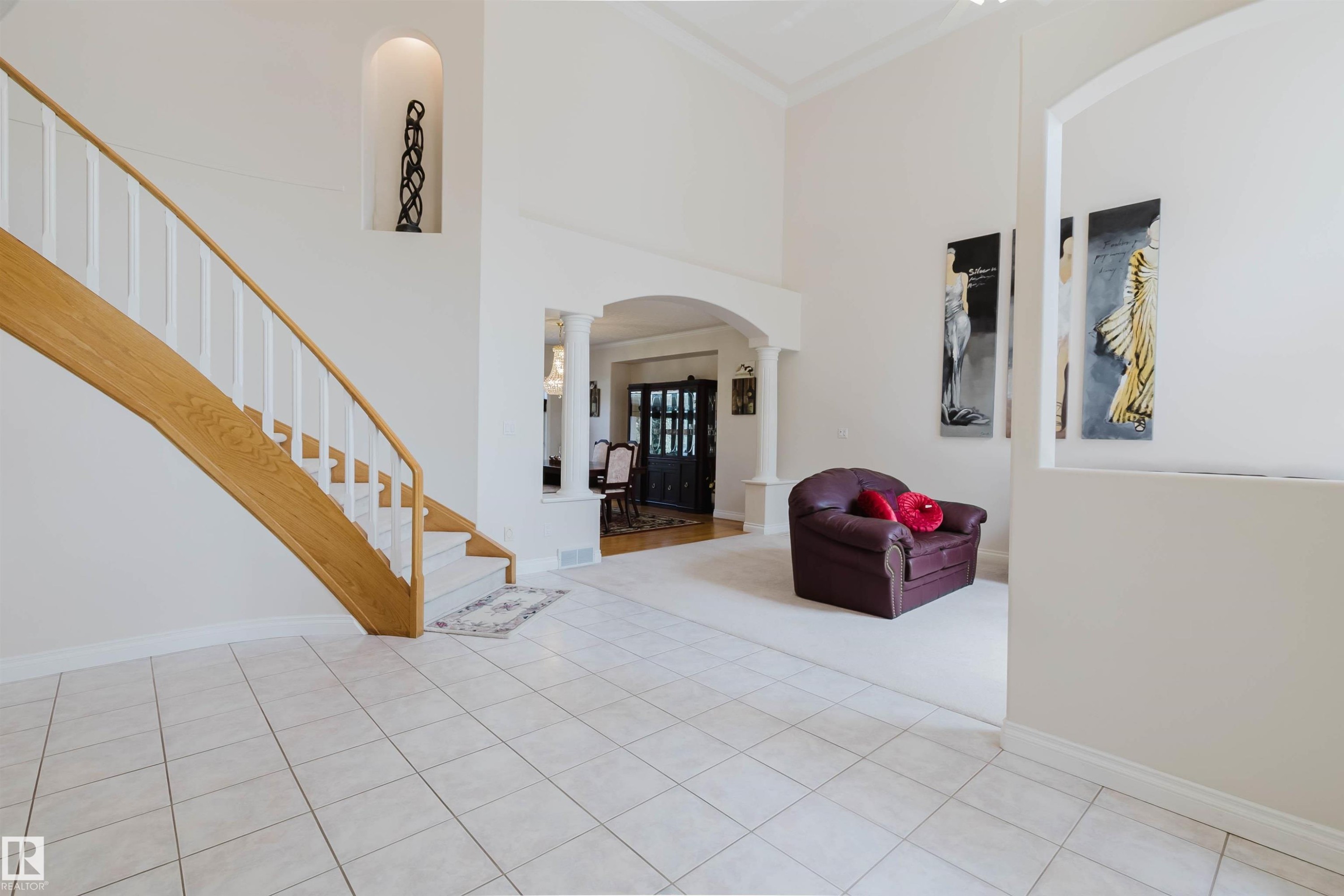 Spacious foyer featuring light-toned square tile flooring, a prominent wooden staircase with white balusters, and a wall niche - 928 Heacock Road Nw, Edmonton, AB - Indoor Photo Showing Other Room