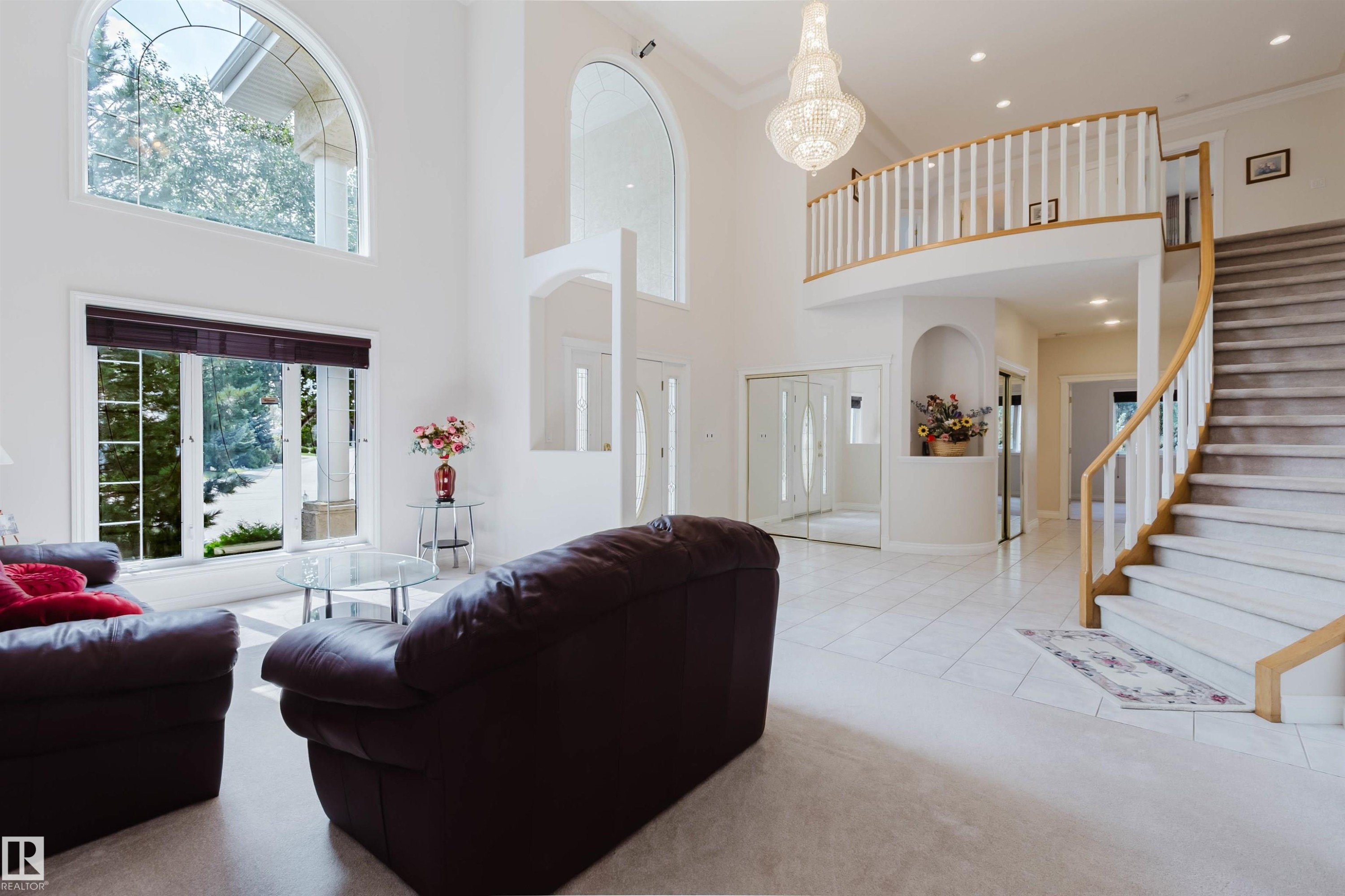 Two-story foyer featuring a grand curved staircase with carpeted treads, a second-story balcony, and an ornate chandelier - 928 Heacock Road Nw, Edmonton, AB - Indoor