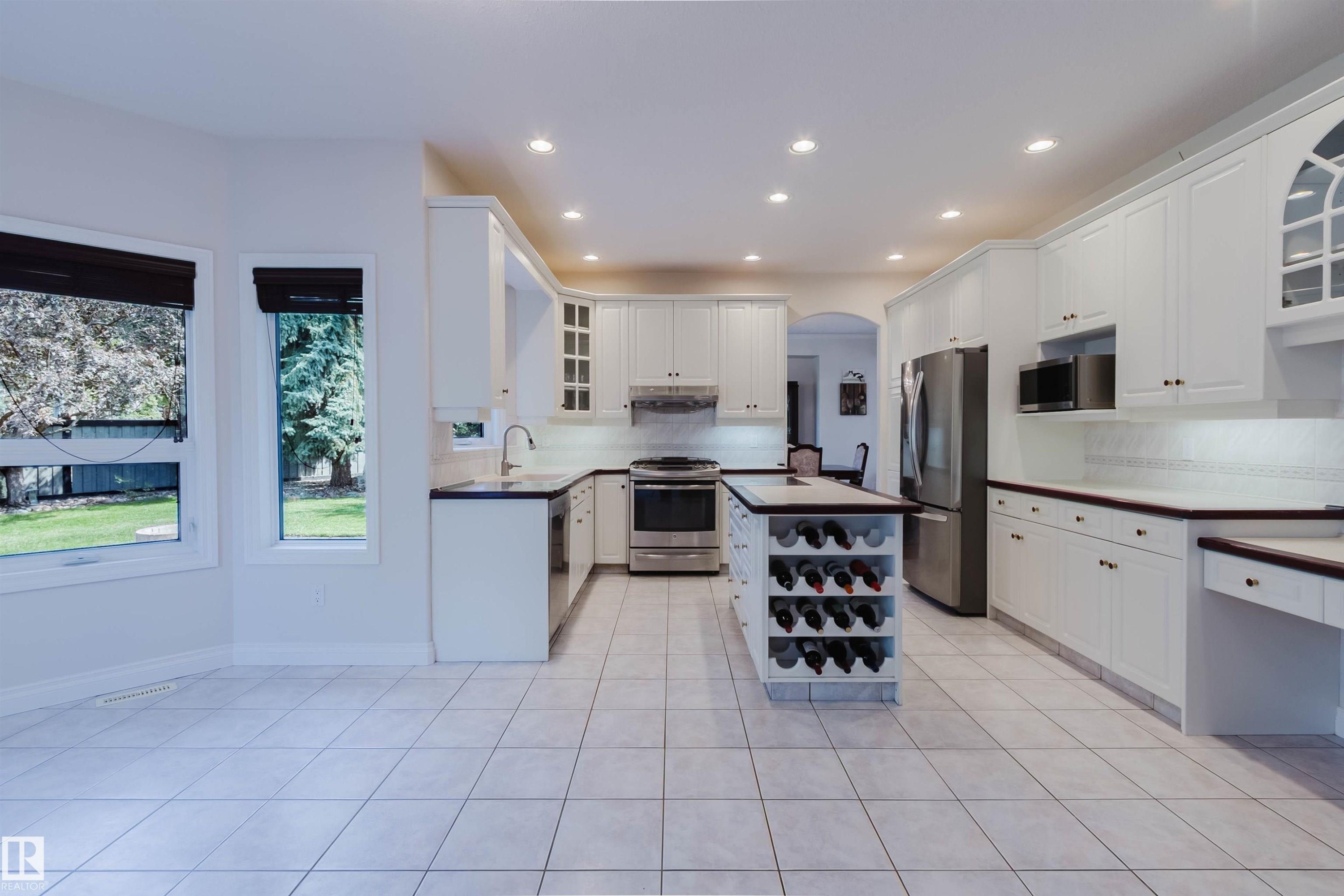 Spacious kitchen featuring white cabinetry, dark countertops, stainless steel appliances, a central island with integrated wine storage, and recessed lighting - 928 Heacock Road Nw, Edmonton, AB - Indoor Photo Showing Kitchen