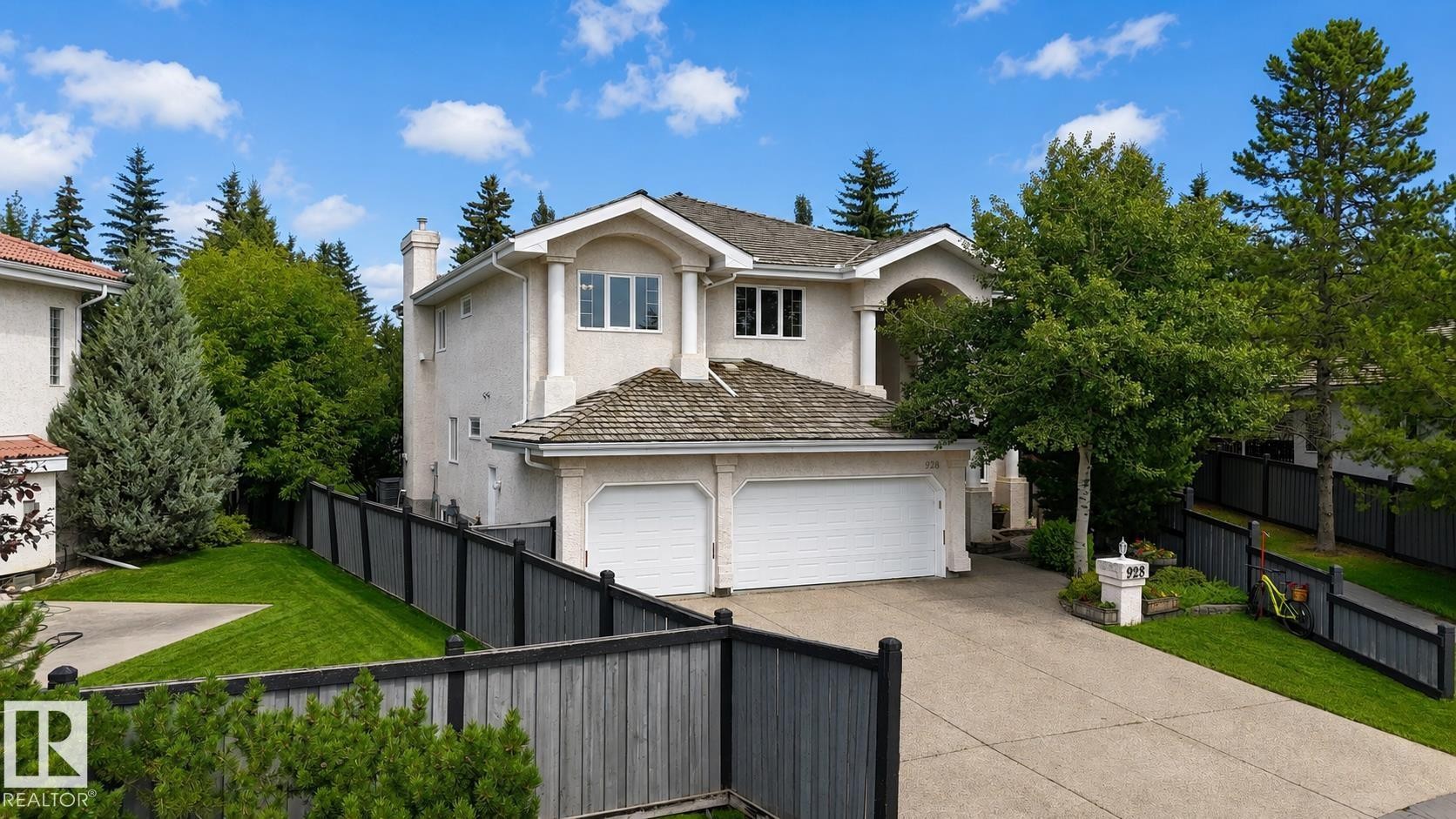 Stucco exterior property featuring an attached two-car garage, concrete driveway, and mature landscaping - 928 Heacock Road Nw, Edmonton, AB - Outdoor