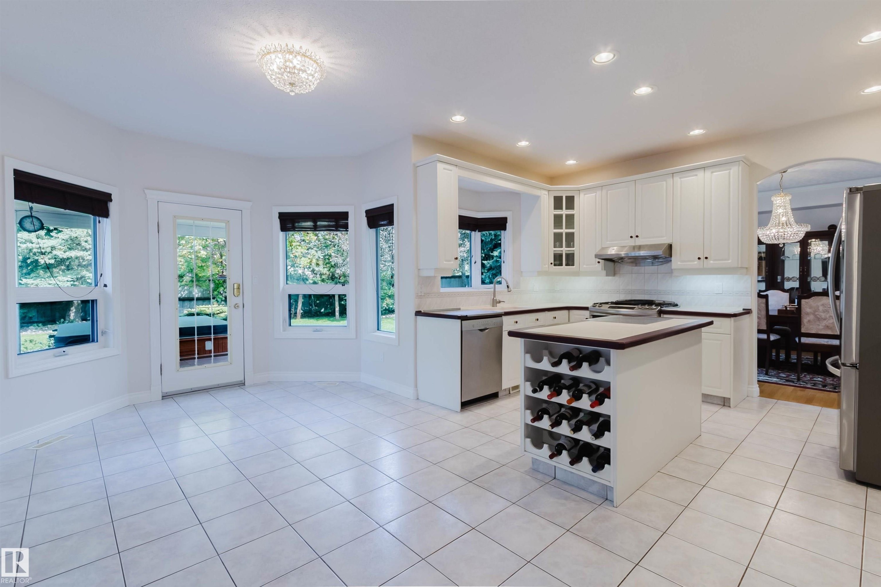 Bright kitchen with white cabinetry, tile flooring, recessed lighting, a central island with integrated wine storage, and a glass-paneled exterior door - 928 Heacock Road Nw, Edmonton, AB - Indoor Photo Showing Kitchen