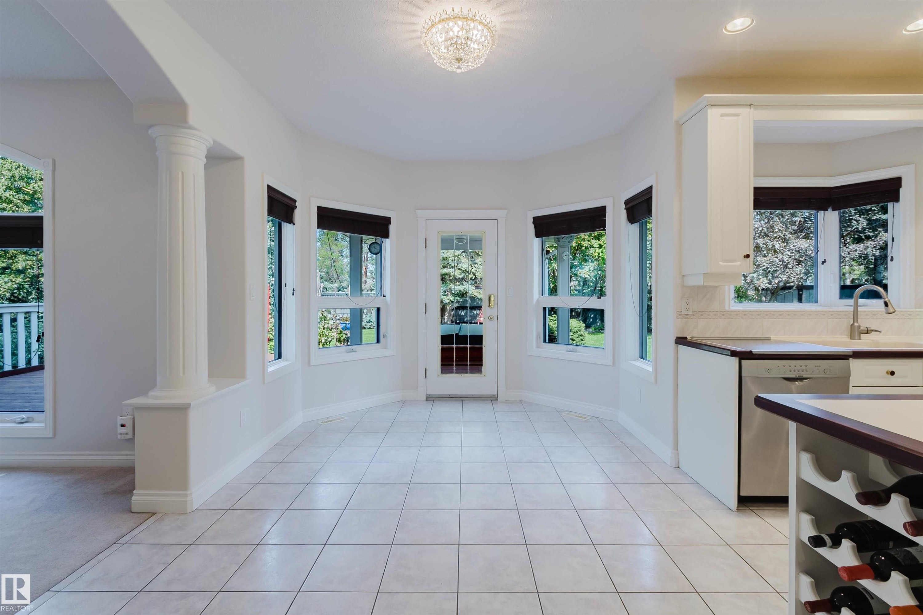Bright dining area featuring tile flooring, multiple windows, a glass-paned exterior door, and an ornate ceiling light fixture - 928 Heacock Road Nw, Edmonton, AB - Indoor