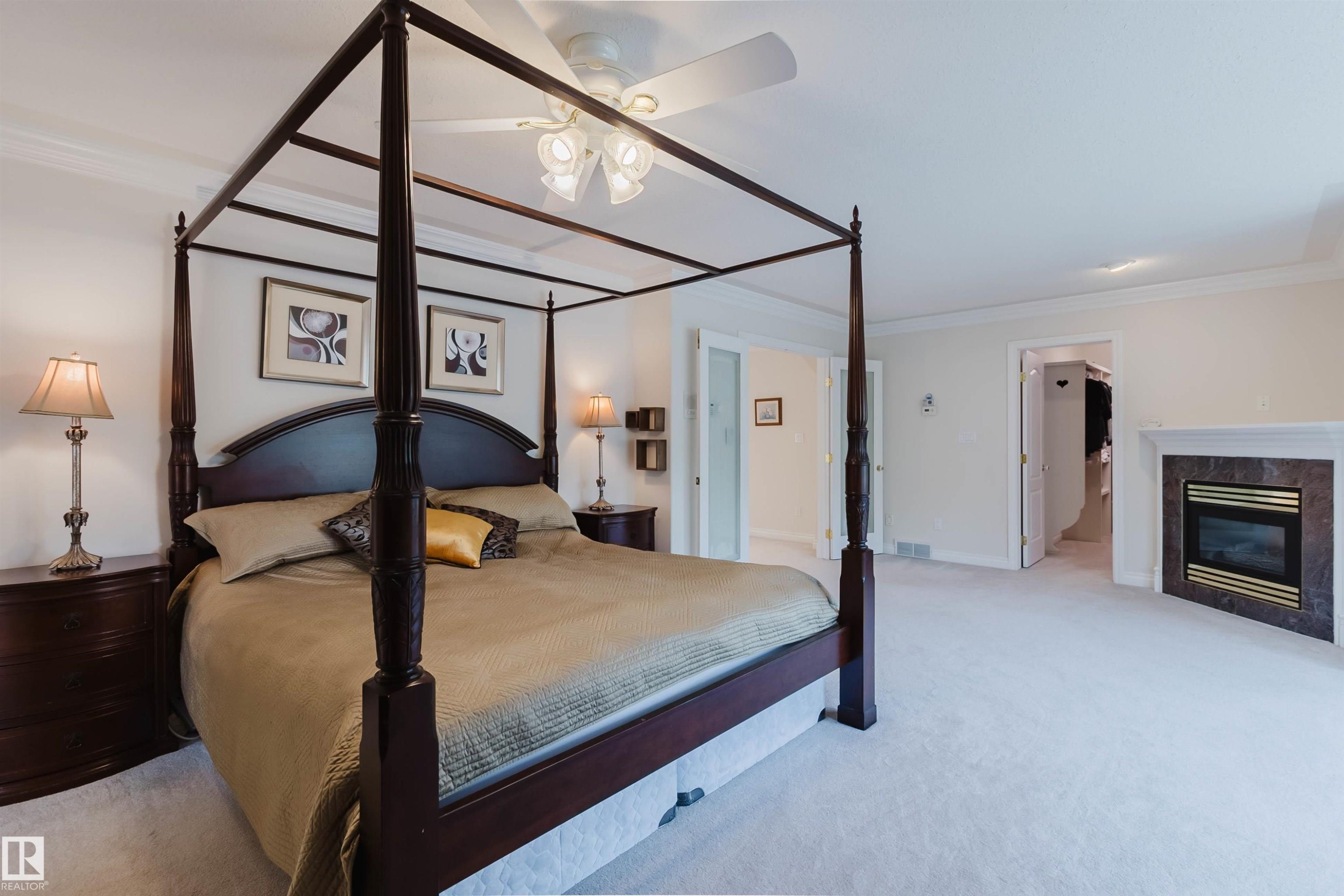 Carpeted room featuring a ceiling fan, crown molding, double door entry, and a built-in fireplace with a stone surround - 928 Heacock Road Nw, Edmonton, AB - Indoor Photo Showing Bedroom