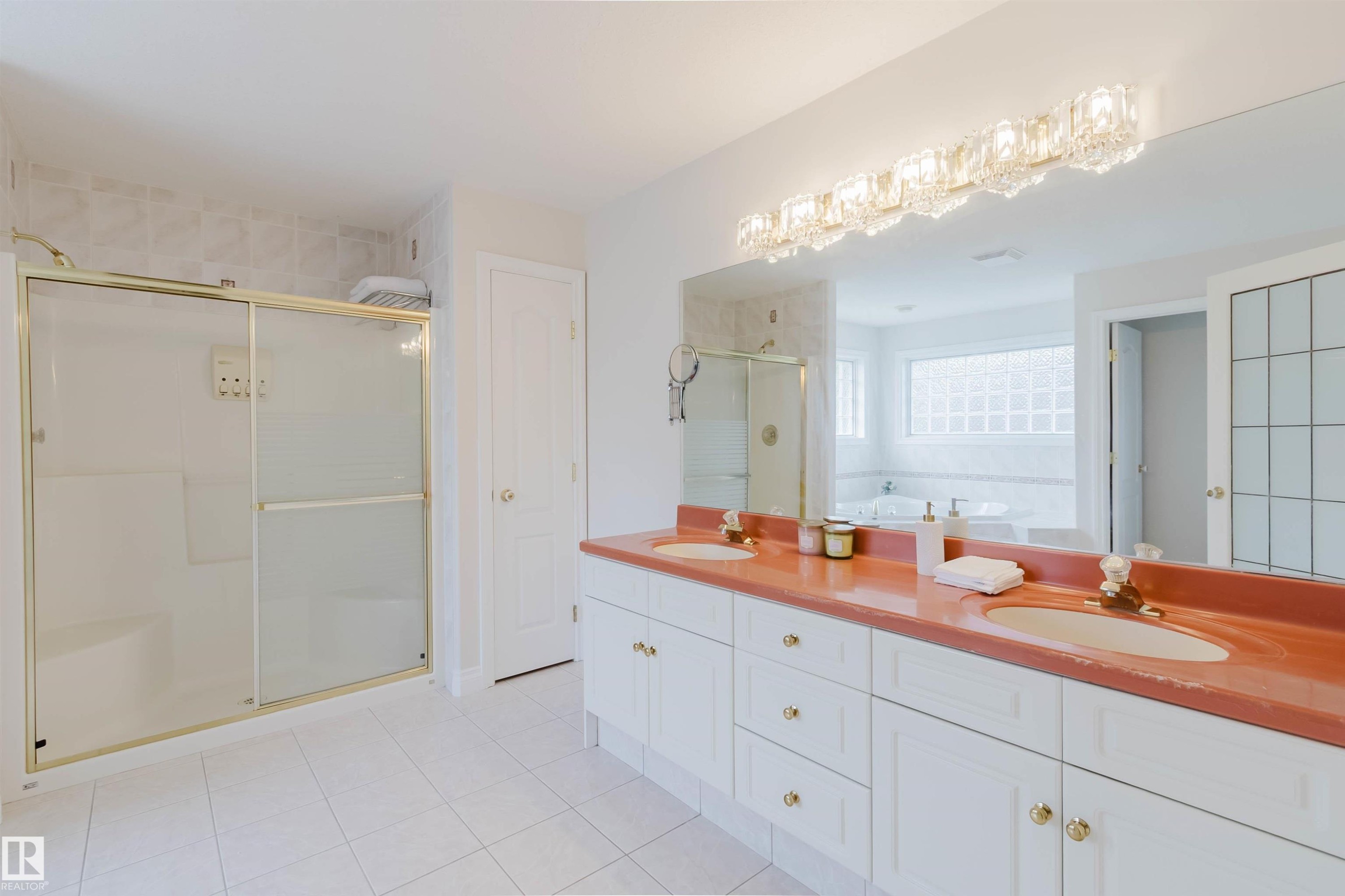 Spacious bathroom featuring a dual vanity with a coral-toned countertop, a large mirror, and an ornate crystal light fixture - 928 Heacock Road Nw, Edmonton, AB - Indoor Photo Showing Bathroom