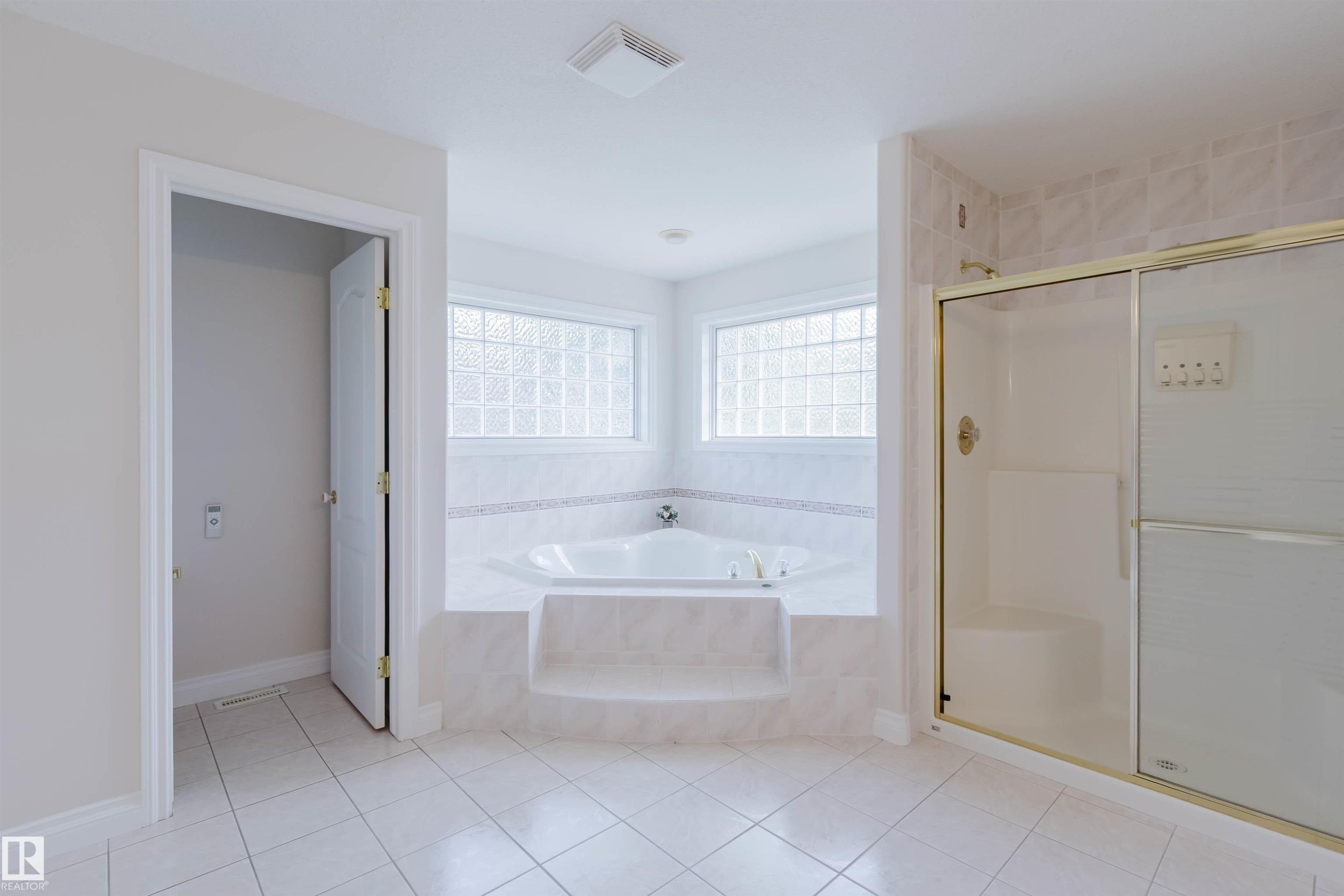 Spacious bathroom featuring a corner soaking tub with tiled surround, glass block windows, and a separate shower enclosure with gold-tone accents - 928 Heacock Road Nw, Edmonton, AB - Indoor Photo Showing Bathroom