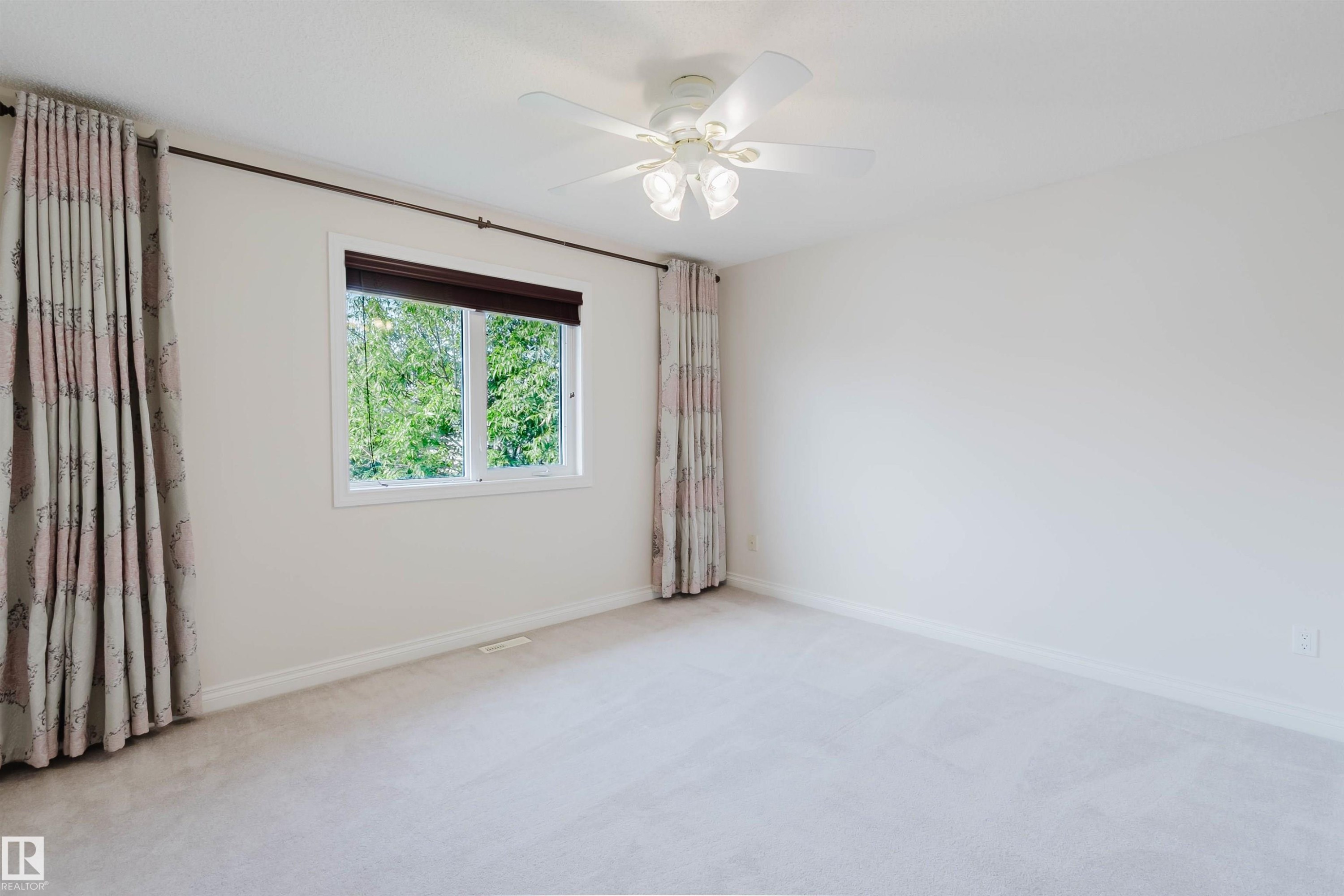 Bright room featuring a window with a dark roller shade, ceiling fan with integrated lighting, wall-to-wall carpeting, and neutral wall tones - 928 Heacock Road Nw, Edmonton, AB - Indoor Photo Showing Other Room