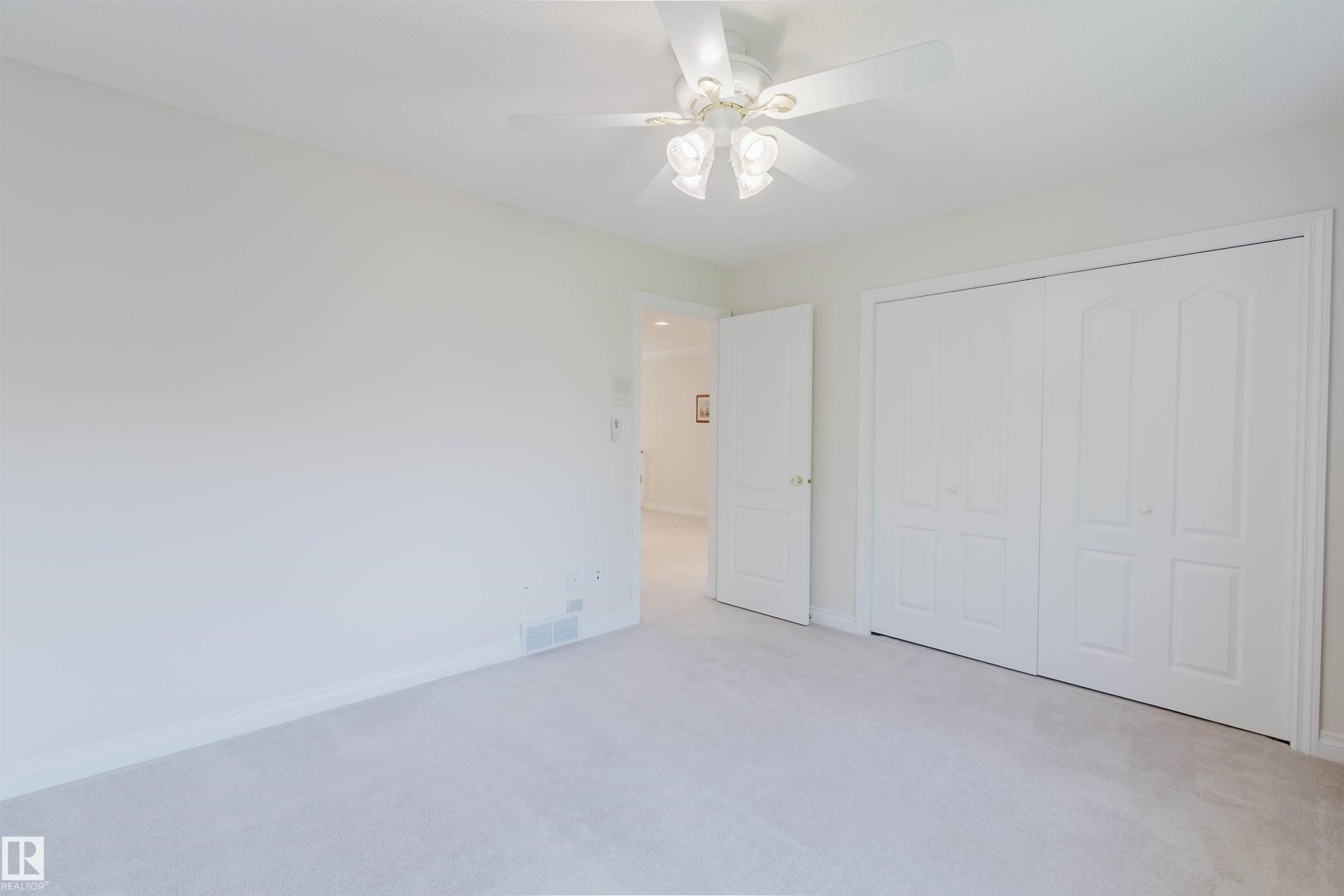 Carpeted room featuring a ceiling fan with light fixture, white walls, and a pair of bi-fold closet doors - 928 Heacock Road Nw, Edmonton, AB - Indoor Photo Showing Other Room