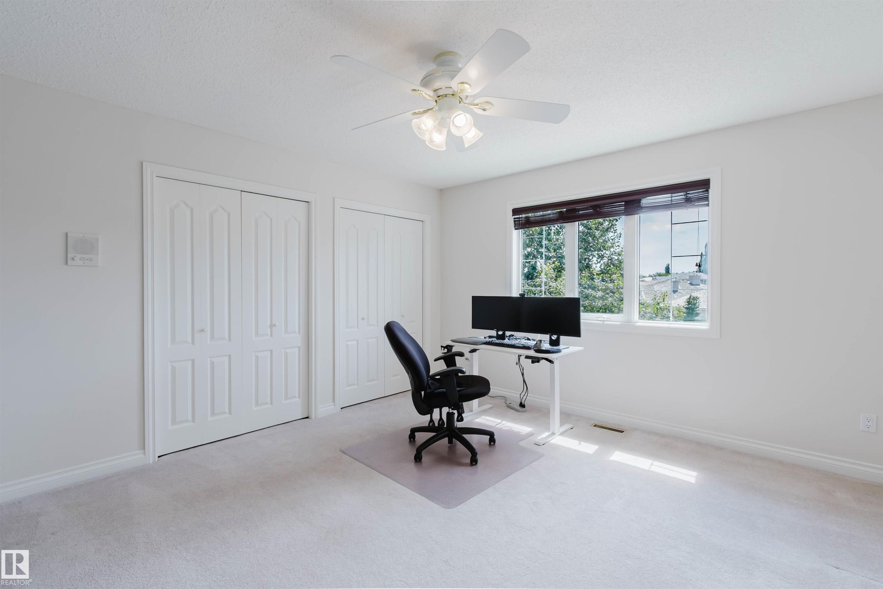 Carpeted room featuring a ceiling fan with integrated lighting, a large window with horizontal blinds, and two sets of bi-fold closet doors - 928 Heacock Road Nw, Edmonton, AB - Indoor Photo Showing Office