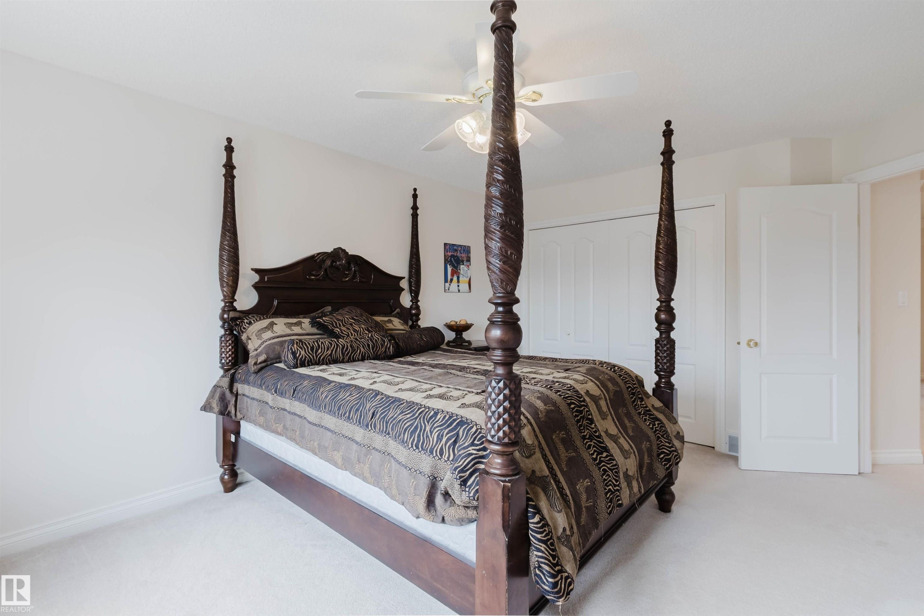 Elegant primary bedroom featuring a striking four-poster bed with ornate carved finials and detailed headboard, anchored by a ceiling-mounted light fixture - 928 Heacock Road Nw, Edmonton, AB - Indoor Photo Showing Bedroom