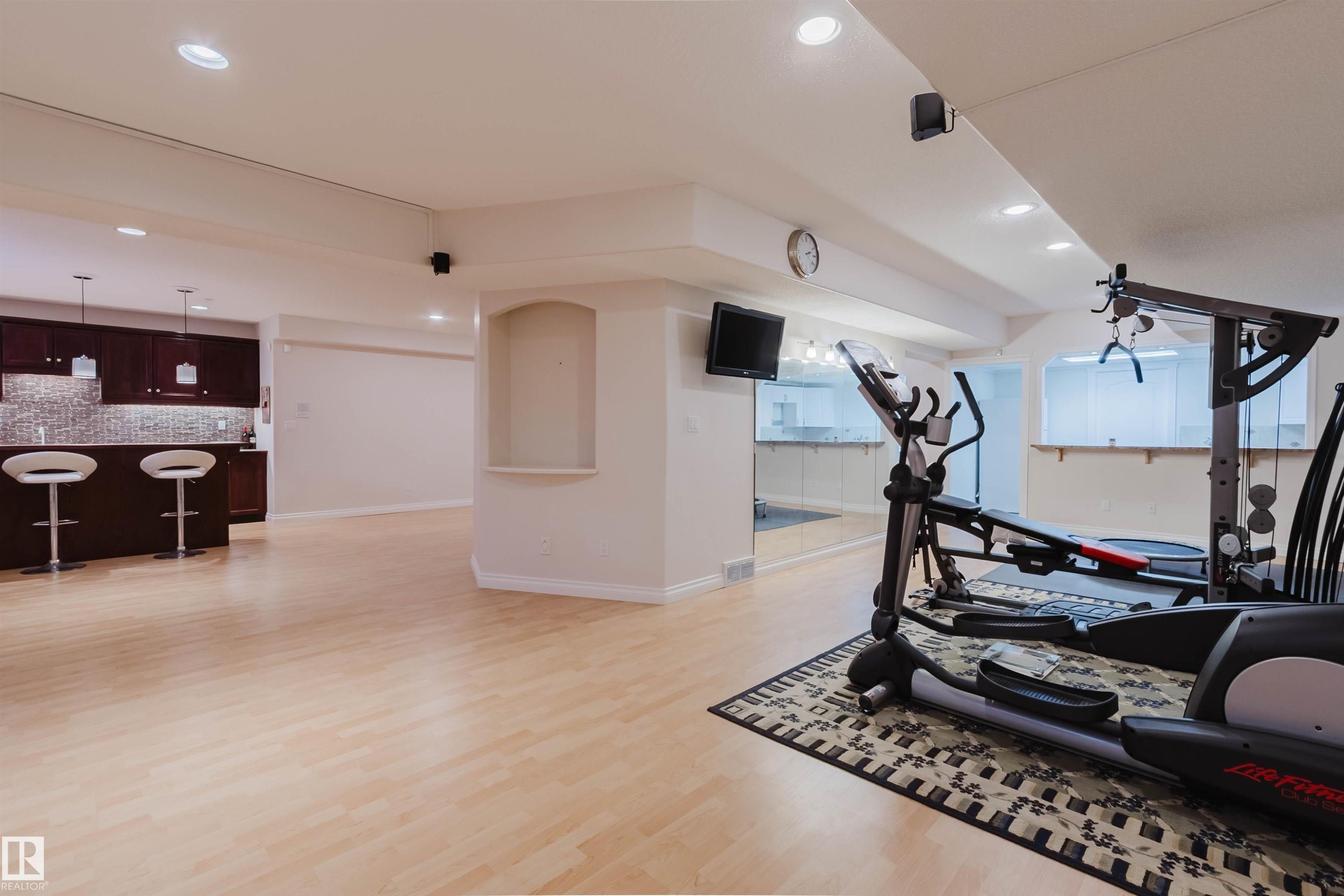 Spacious lower level featuring light wood-finish flooring, recessed lighting, and a built-in wet bar with dark wood cabinetry - 928 Heacock Road Nw, Edmonton, AB - Indoor Photo Showing Gym Room