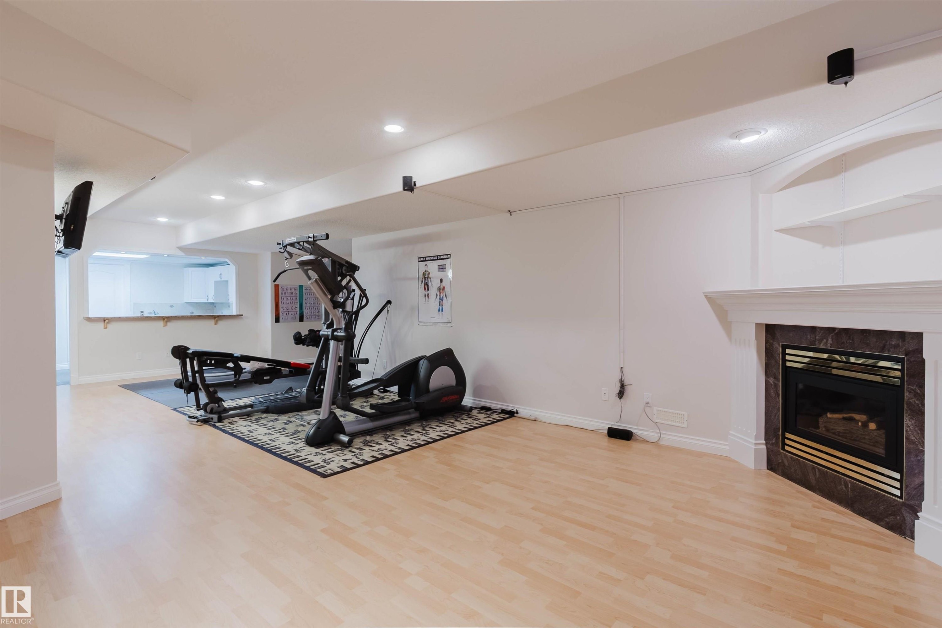 Spacious recreational room featuring light wood-finish flooring, recessed lighting, and a corner fireplace with a dark stone surround and white mantel - 928 Heacock Road Nw, Edmonton, AB - Indoor With Fireplace