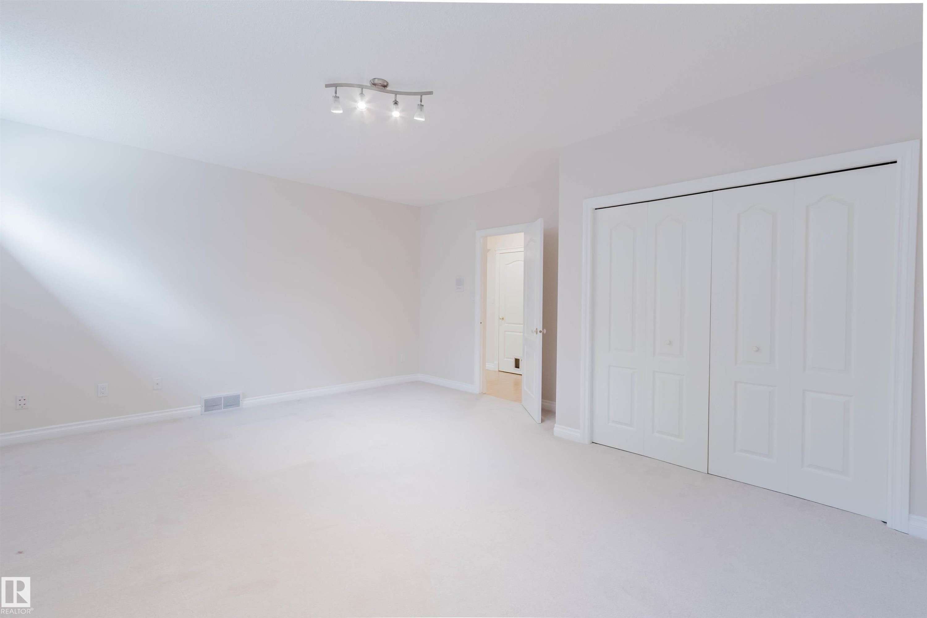 Carpeted room featuring white walls, a track light fixture, and a white bi-fold closet with panel details - 928 Heacock Road Nw, Edmonton, AB - Indoor