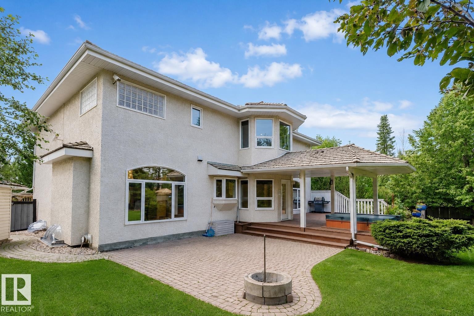 Rear exterior featuring a covered deck, stone paver patio, integrated hot tub, and manicured lawn - 928 Heacock Road Nw, Edmonton, AB - Outdoor With Deck Patio Veranda