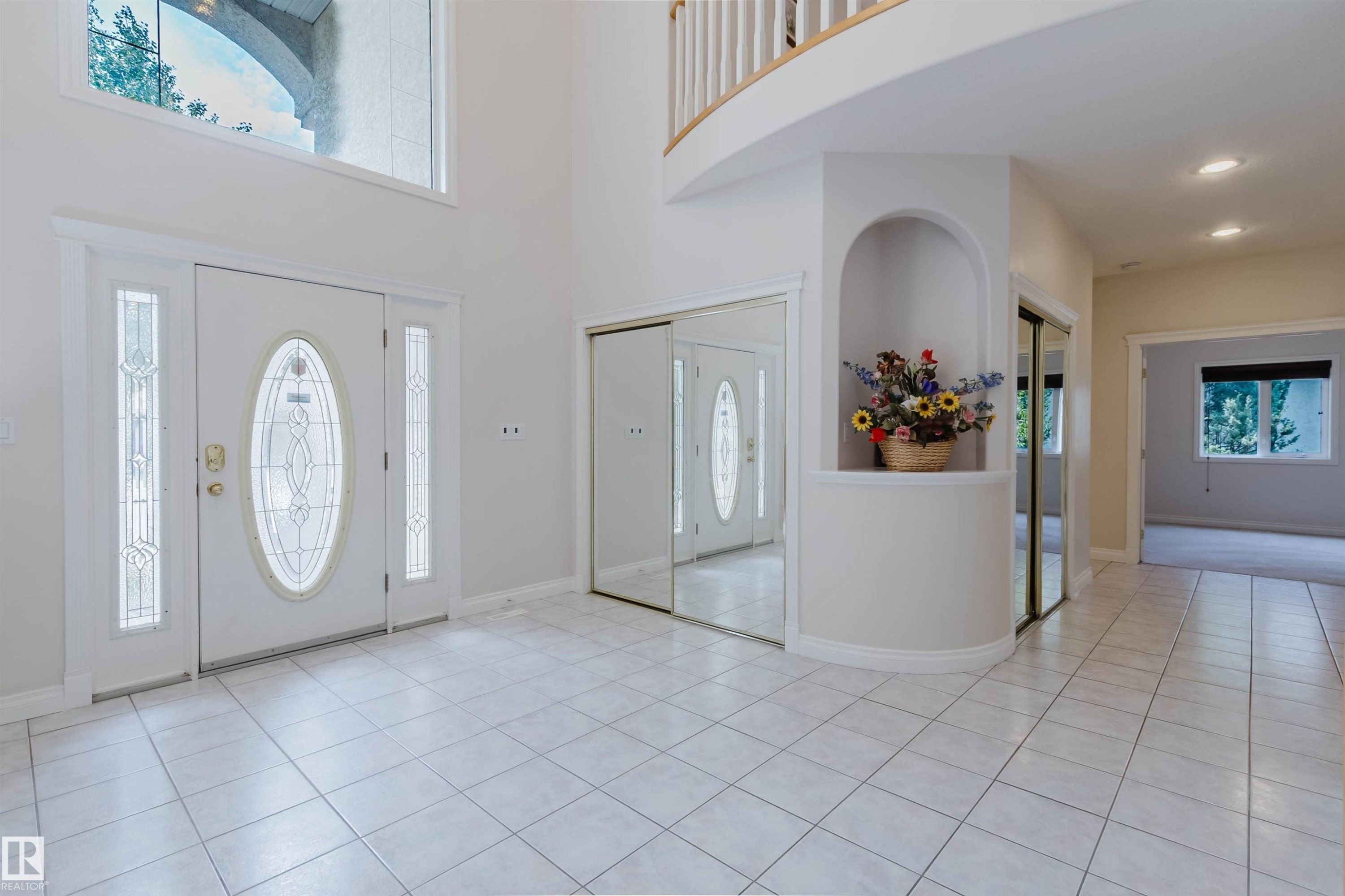 Grand entry foyer featuring a double-height ceiling, large decorative glass entry door with sidelights and transom window, light-toned square tile flooring, and a built-in wall niche - 928 Heacock Road Nw, Edmonton, AB - Indoor Photo Showing Other Room