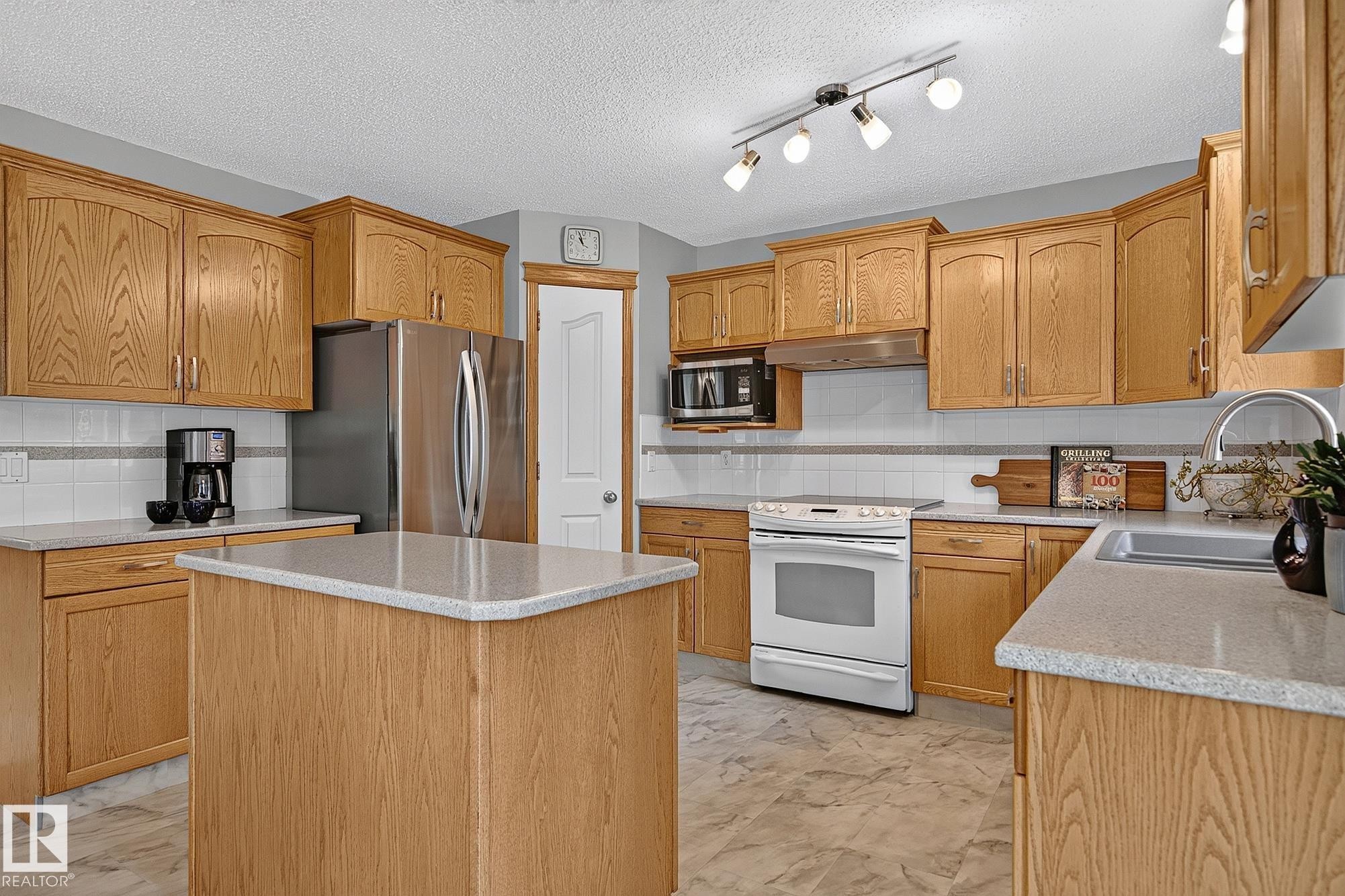 Kitchen featuring wood cabinetry, light-toned countertops, a central island, and vinyl plank flooring - 385 Meadowview Terrace, Sherwood Park, AB - Indoor Photo Showing Kitchen