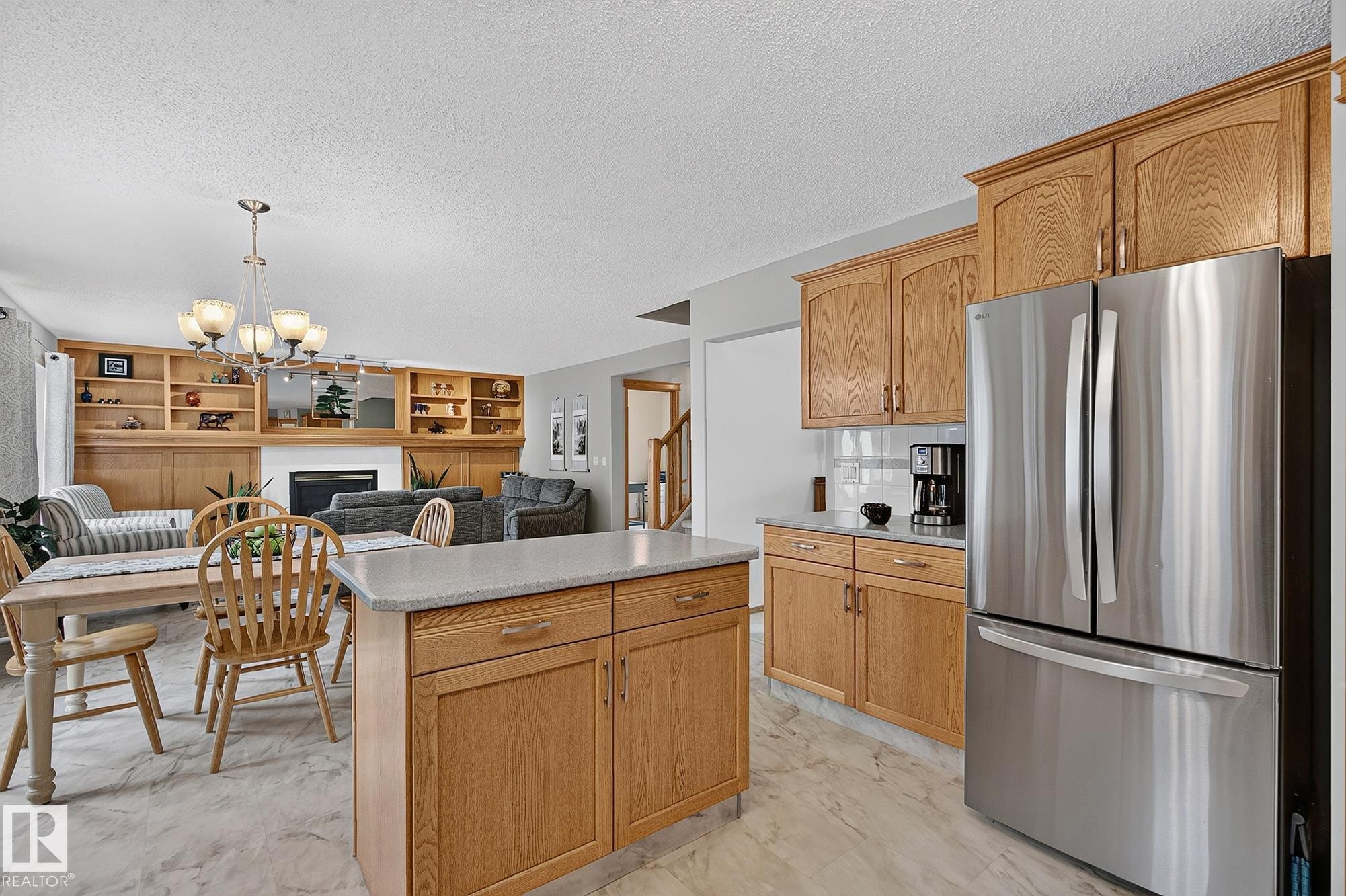 Open-concept kitchen and dining area featuring light wood cabinetry, a central island with a light-toned countertop, stainless steel appliances, and light marble-patterned flooring - 385 Meadowview Terrace, Sherwood Park, AB - Indoor Photo Showing Kitchen