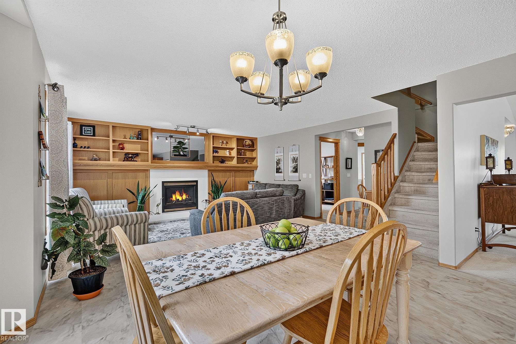 Open-concept living area featuring a built-in wood-finish shelving unit, and natural gas fireplace - 385 Meadowview Terrace, Sherwood Park, AB - Indoor Photo Showing Dining Room With Fireplace