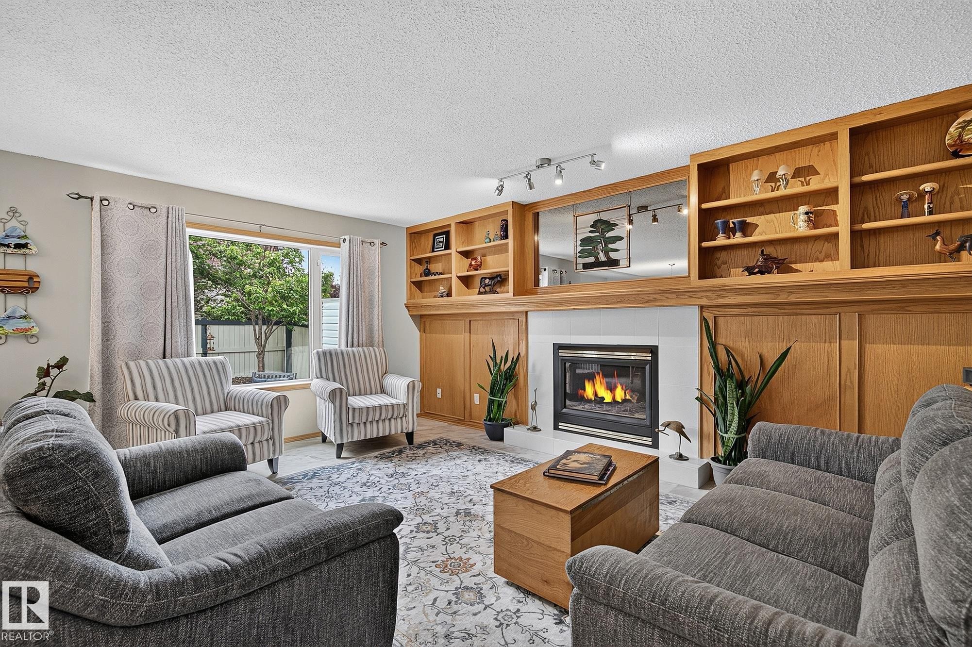 Gas fireplace in the south-facing family room with white tile surround and recessed lighting, flanked by built-in wood shelving and cabinetry - 385 Meadowview Terrace, Sherwood Park, AB - Indoor Photo Showing Living Room With Fireplace