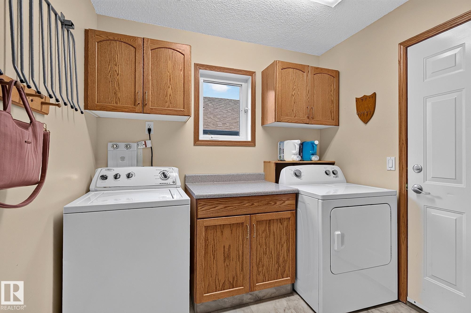 Garage entry and laundry space featuring a window, wood-finish cabinetry, and solid surface countertops - 385 Meadowview Terrace, Sherwood Park, AB - Indoor Photo Showing Laundry Room