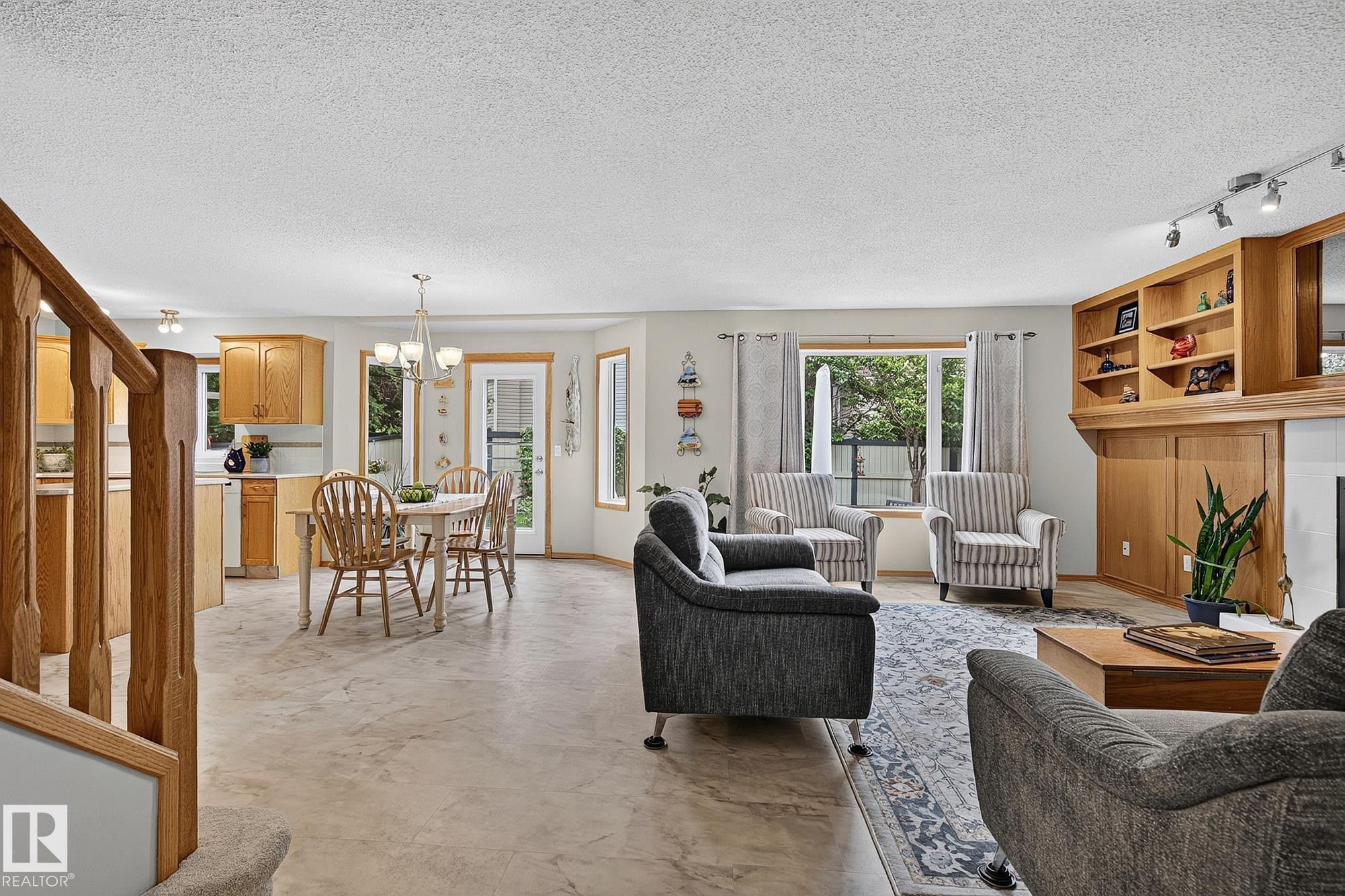 Open-concept living space featuring wood-finish flooring throughout, a kitchen with light wood cabinetry, and a eating area with a glass-paned door leading to the back yard - 385 Meadowview Terrace, Sherwood Park, AB - Indoor Photo Showing Living Room With Fireplace